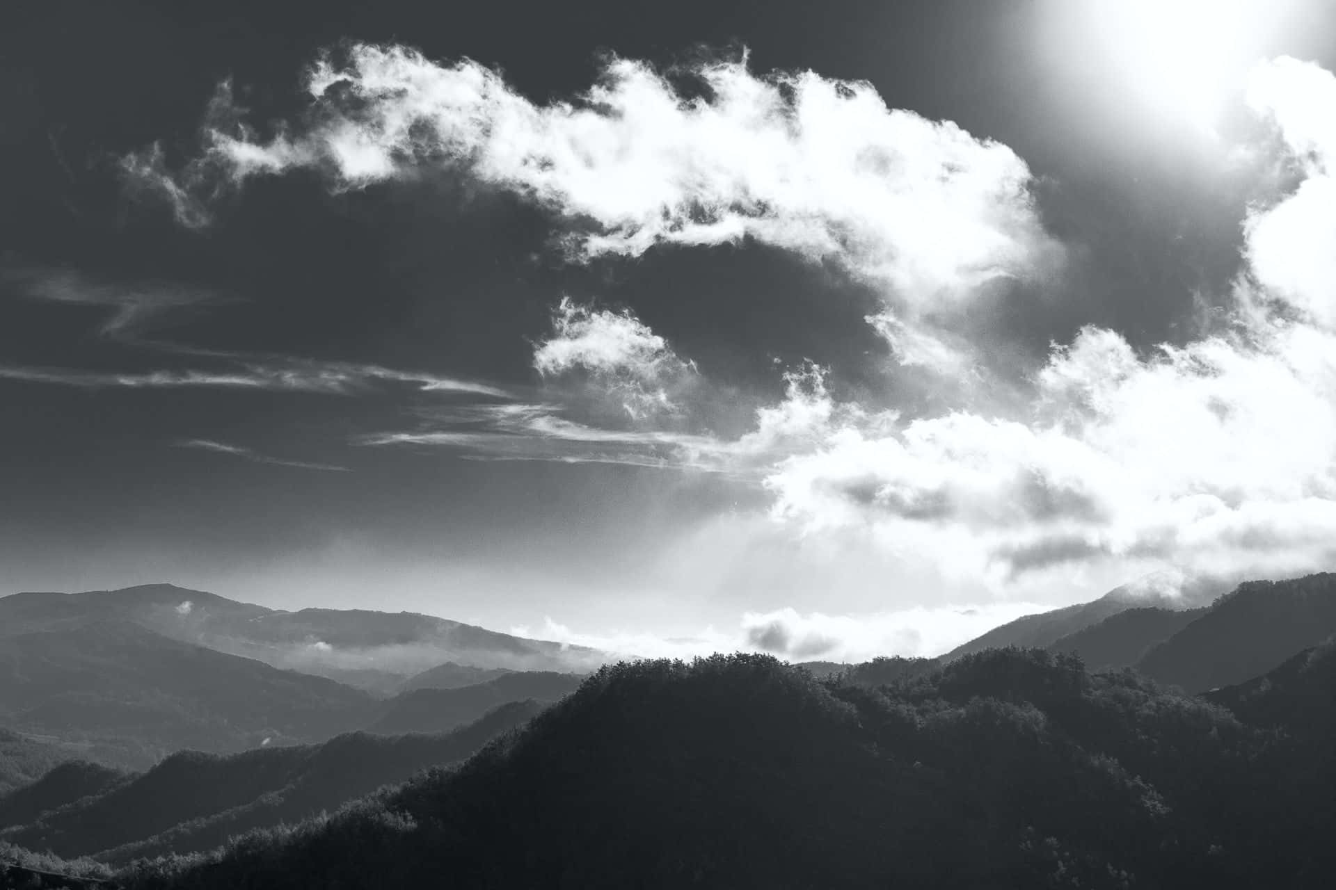 Black And White Sky 桌布 壁紙 — 戲劇性的黑白山景，陽光照射的雲層在層疊的山峰上投下陰影。