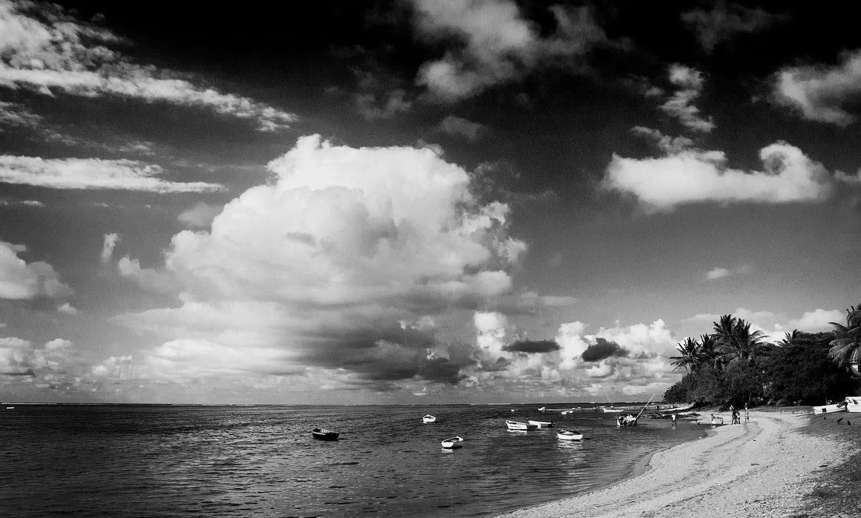 Black And White Landscape 桌布 壁紙 — 戲劇性的黑白海岸場景，船隻點綴在平靜的水面上，天空佈滿紋理豐富的雲層。