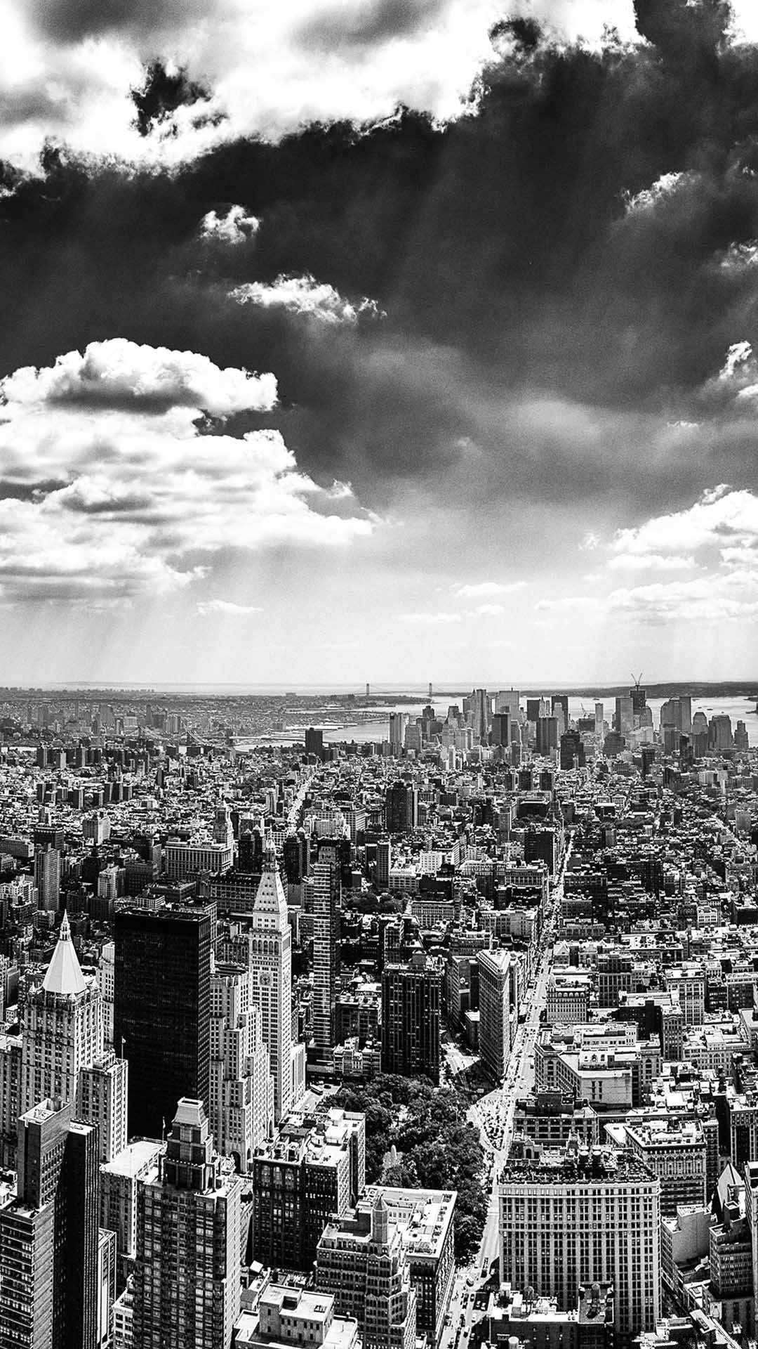 Black And White iPhone 桌布 壁紙 — 戲劇性的黑白空中俯瞰密集的城市天際線，高聳的摩天大樓和雲層投射出光線。