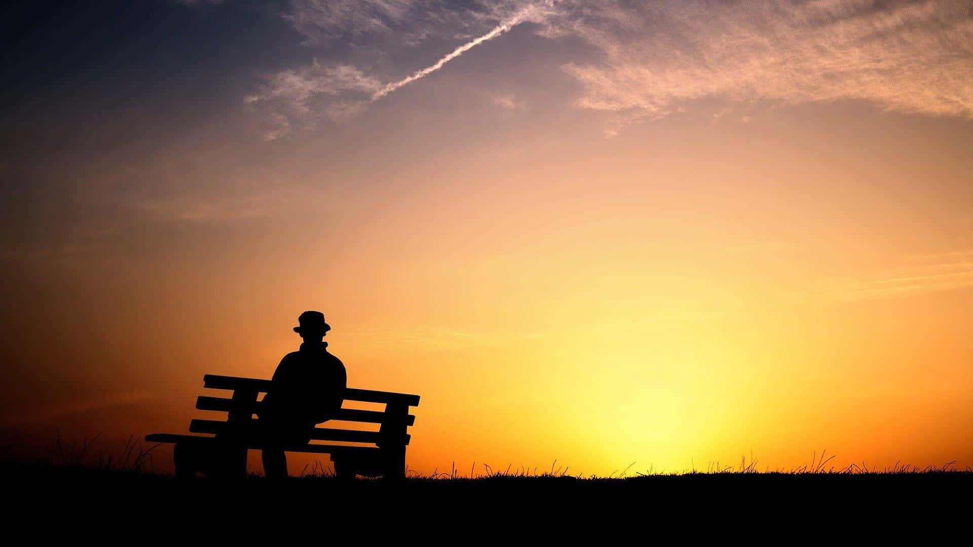 Silhouette 桌布 壁紙 — 戴帽人物的剪影獨自坐在長椅上，觀看夕陽落在草地上。