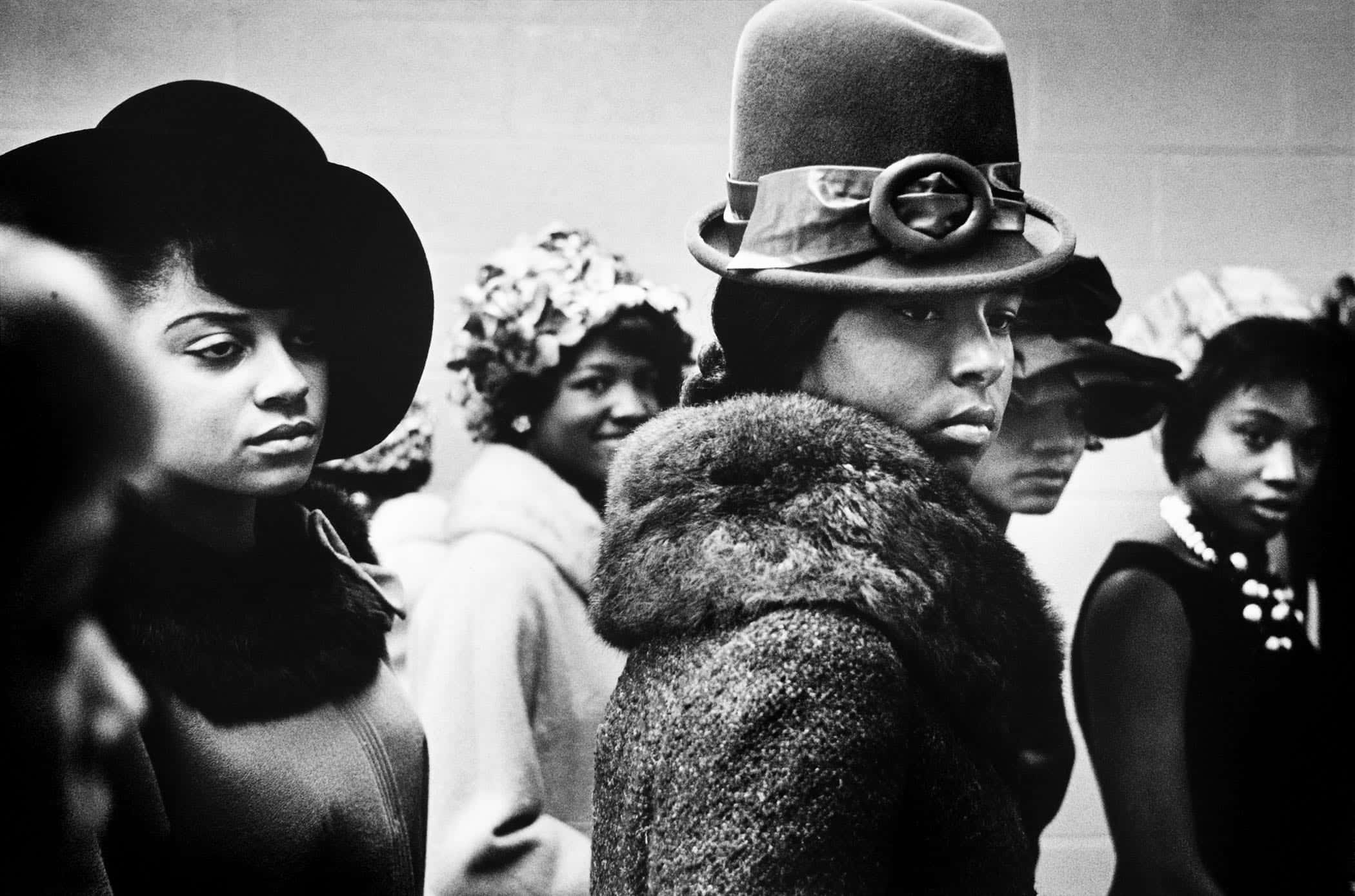 Black Culture 桌布 壁紙 — 戴帽子和外套的時尚女性排成一排，表情嚴肅的黑白照片。