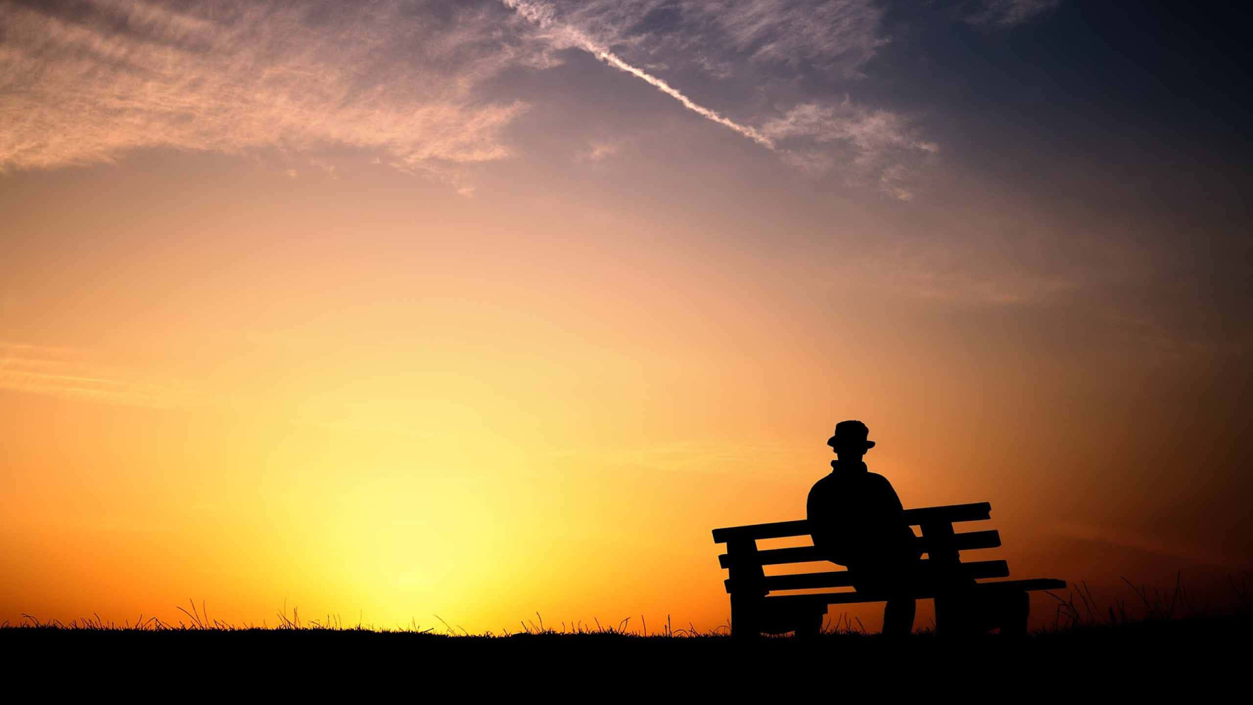 Evening 桌布 壁紙 — 戴帽男子的剪影獨自坐在長椅上，觀賞夕陽落在草地上。