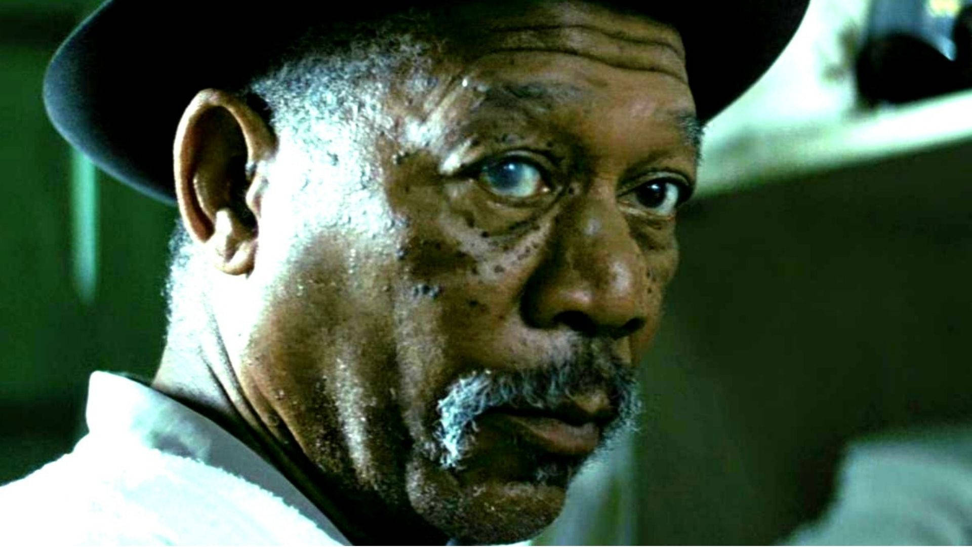 Morgan Freeman 桌布 壁紙 — 戴帽的滄桑男人特寫，在綠色燈光下有一雙強烈的藍色眼睛和灰色鬍鬚。