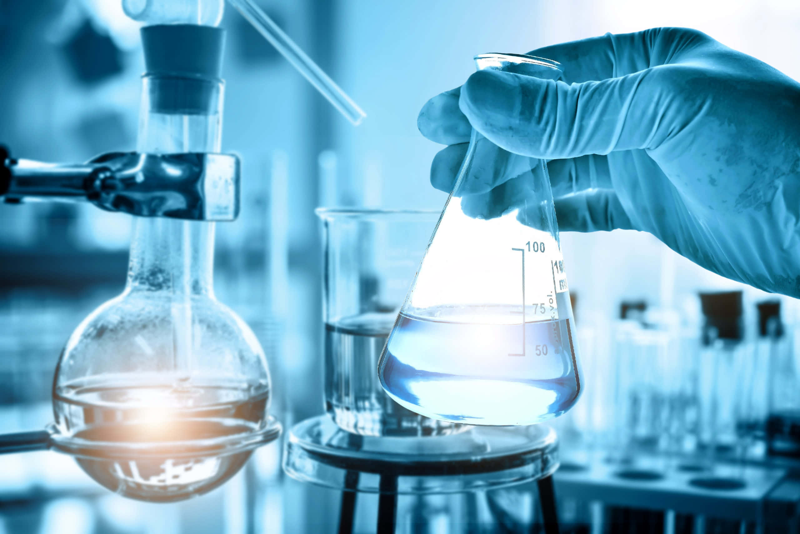 Science Lab 桌布 壁紙 — 戴手套的手在充滿玻璃器皿的冷藍色實驗室中握住一個發光的燒杯。