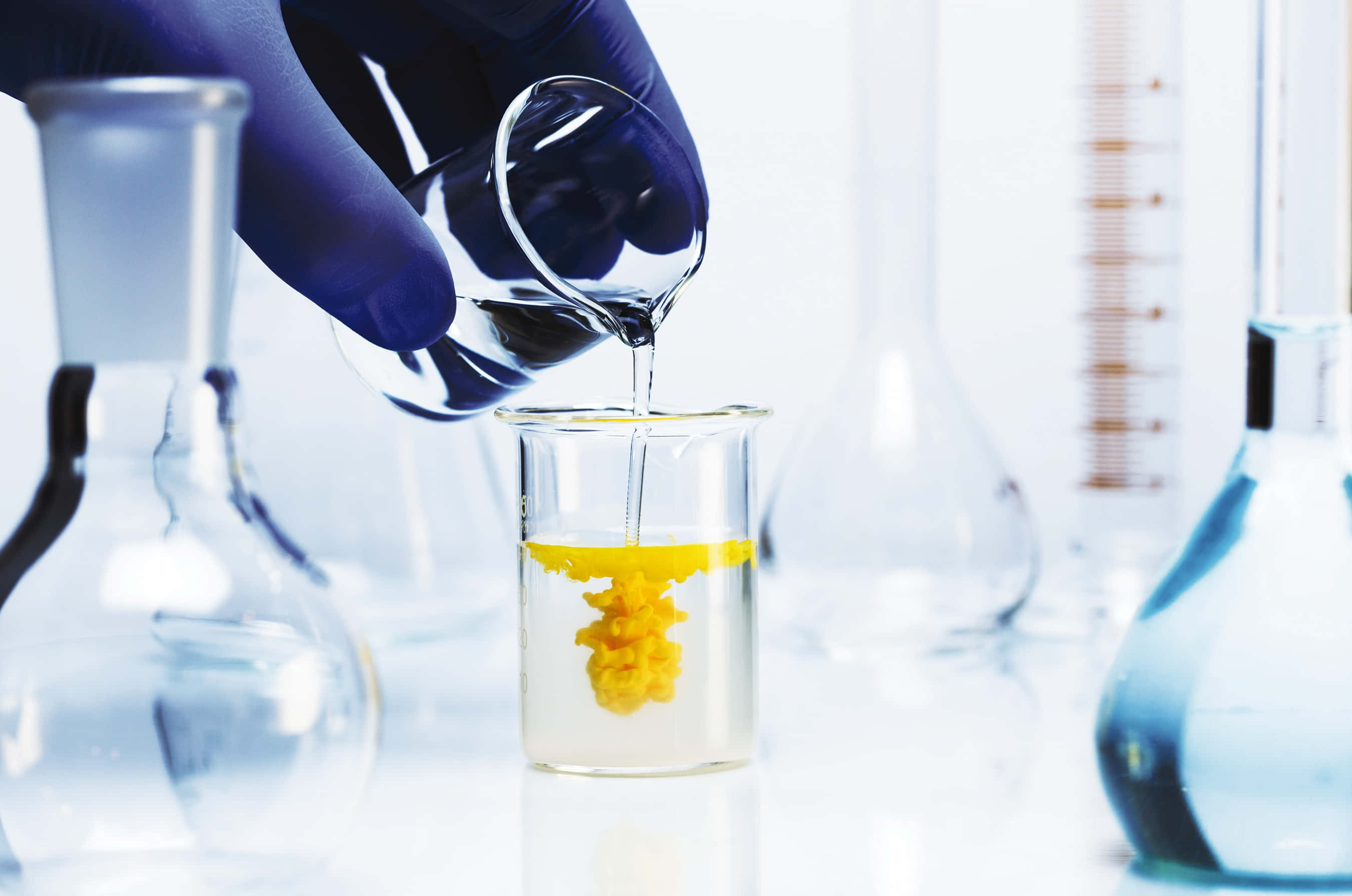 科學 桌布 壁紙 — 戴手套的手在實驗室玻璃器皿中將液體倒入含有黃色結晶物質的燒杯中。