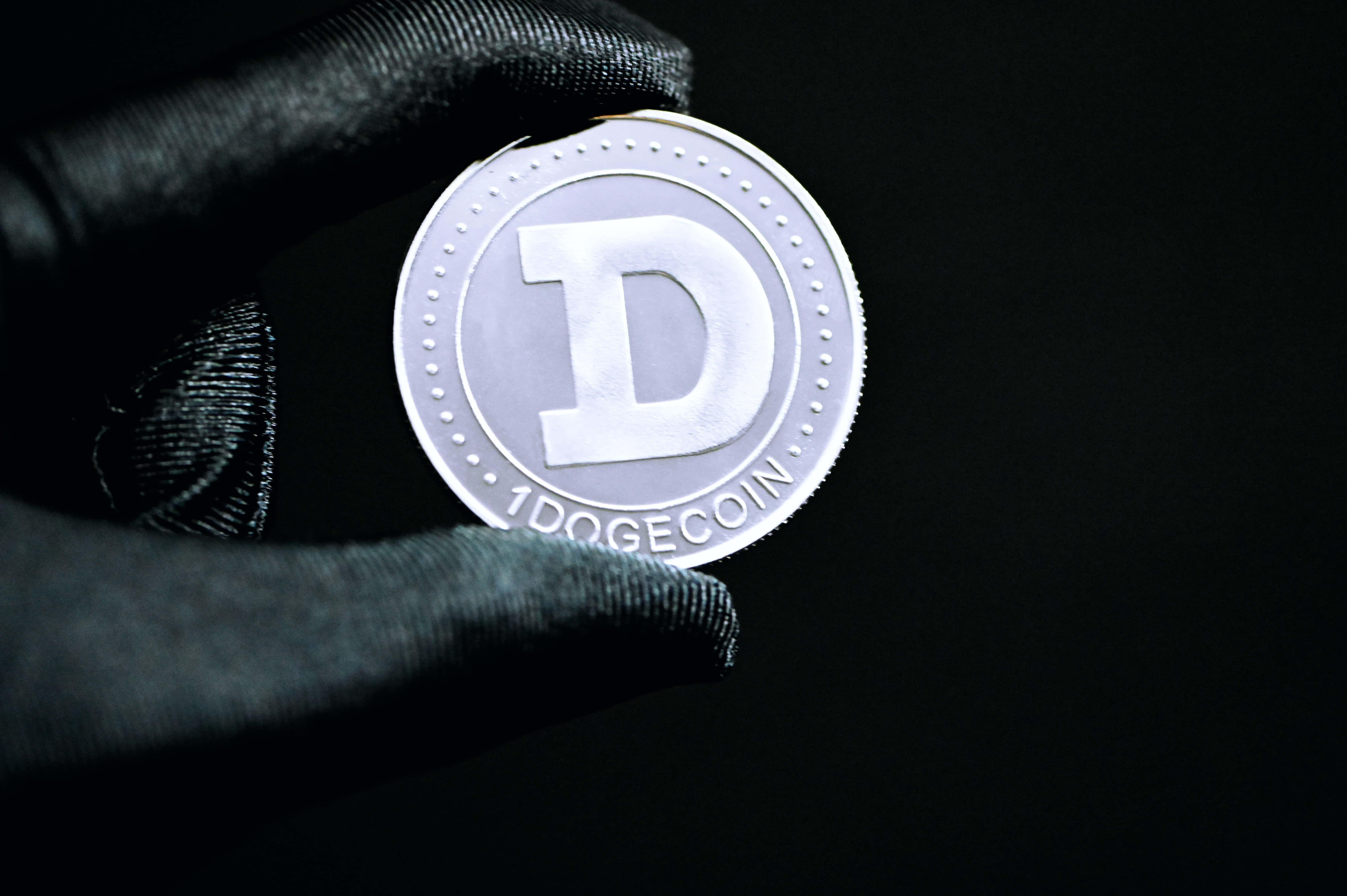 Dogecoin 桌布 壁紙 — 戴手套的手在強烈燈光下，於純黑背景上托著一枚銀色Dogecoin。