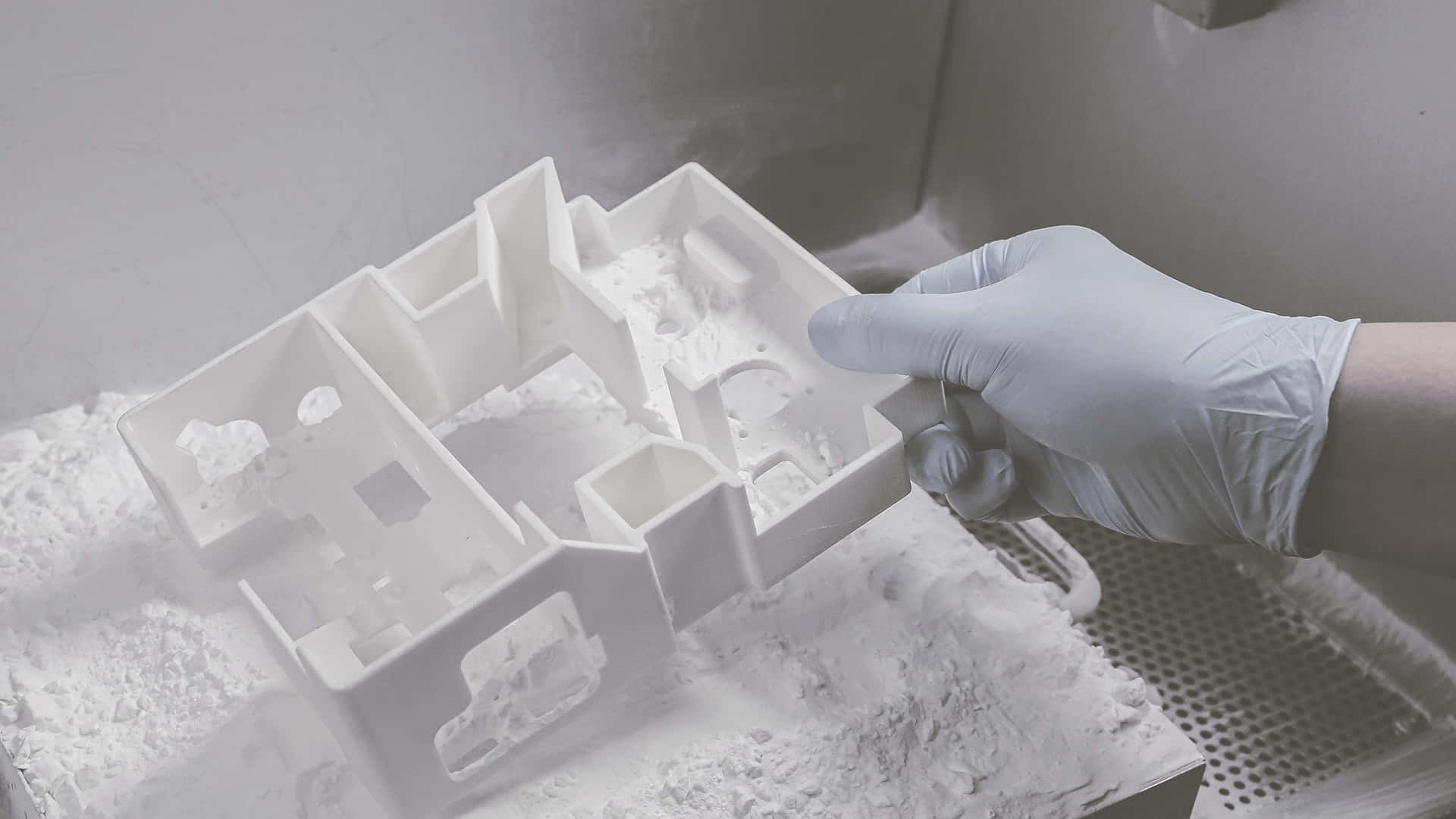 3d Printer 桌布 壁紙 — 戴手套的手從無塵室環境中的粉末床上拿起一個白色3D列印建築模型。
