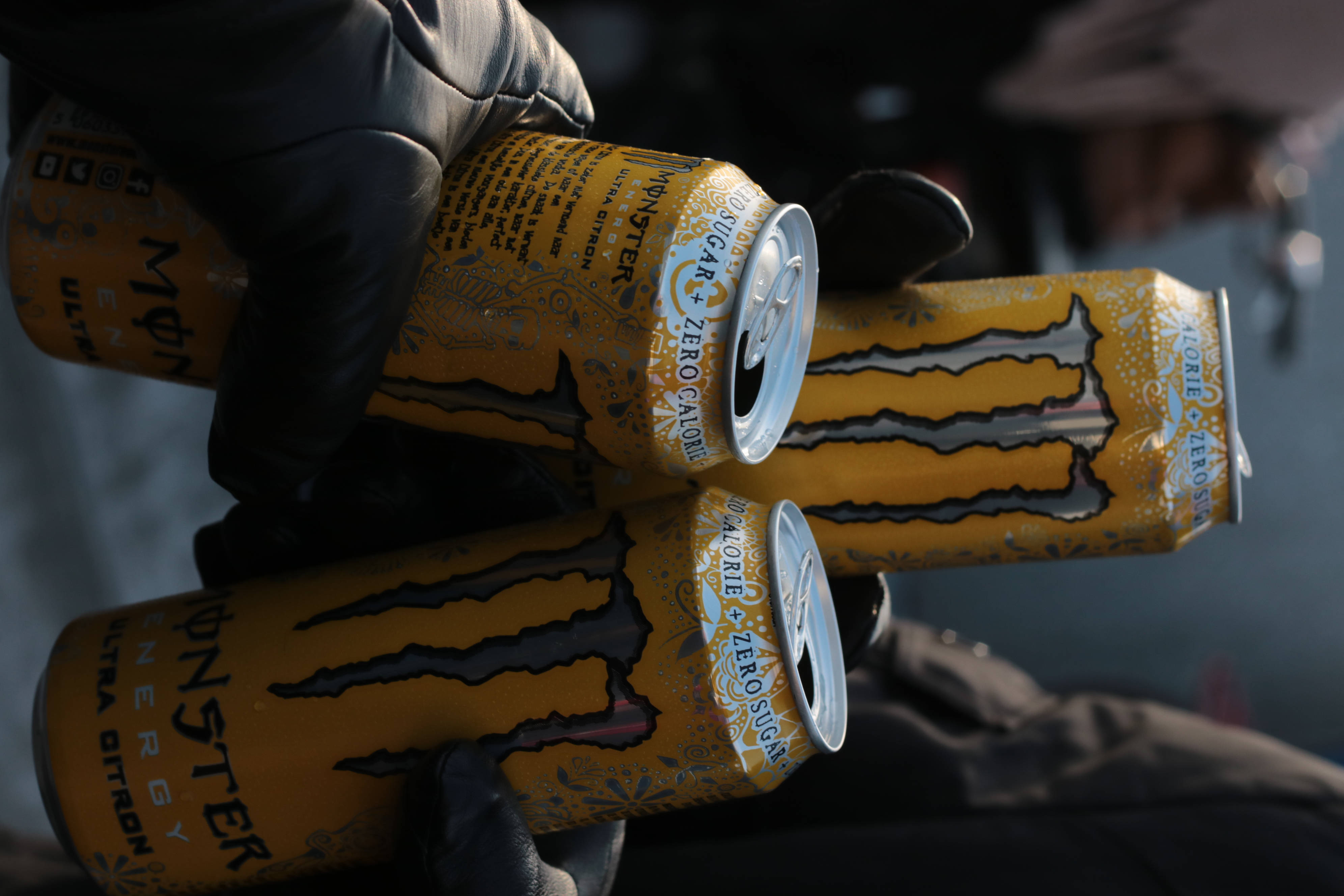 Monster Energy 桌布 壁紙 — 戴手套的手抓住三個黃色Monster Ultra零卡路里能量飲料罐，帶有銀色拉環和黑色爪痕。