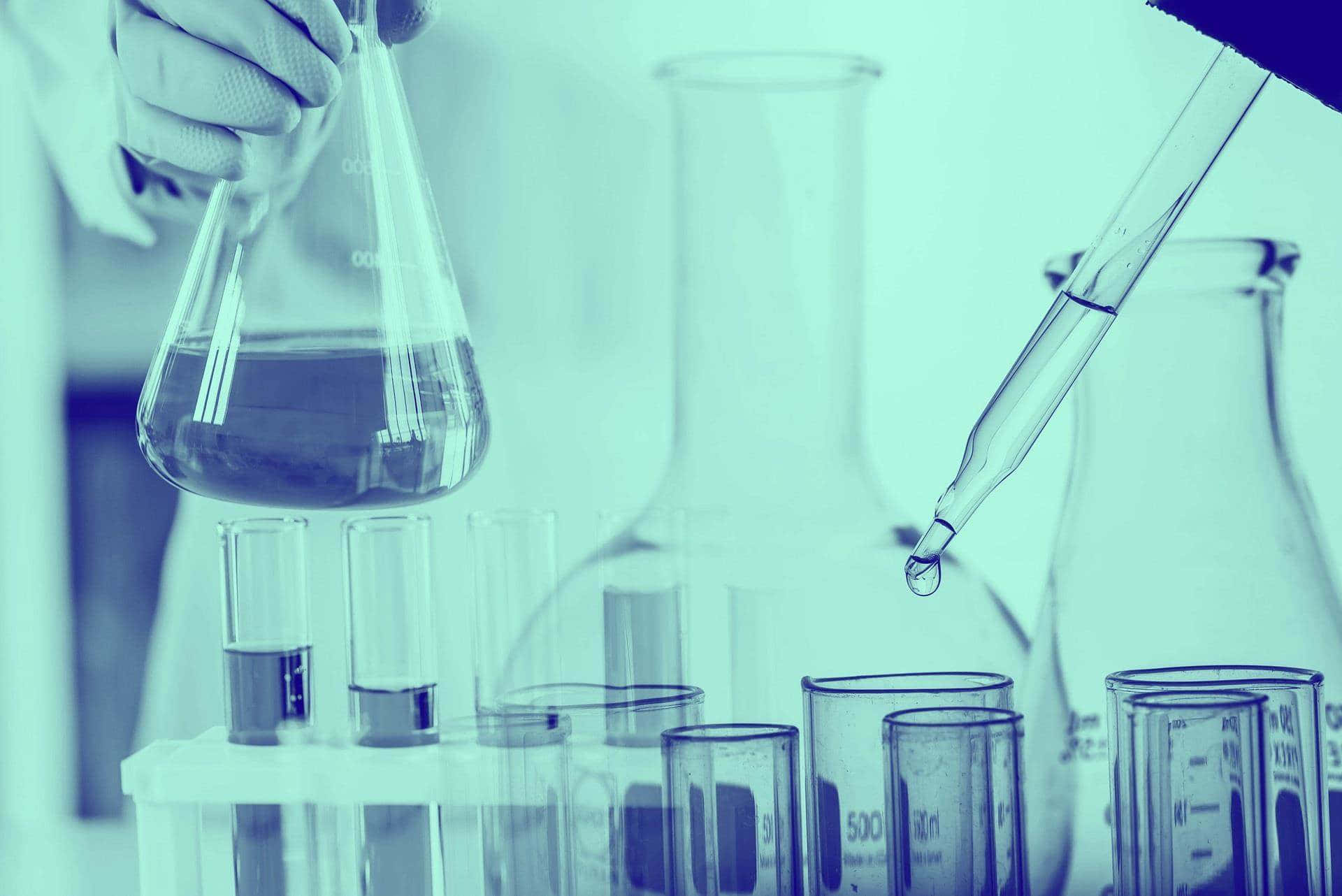 科學 桌布 壁紙 — 戴手套的手拿著錐形瓶，滴管將一滴液體滴入試管中，周圍是實驗室玻璃器皿，在冷藍色燈光下。
