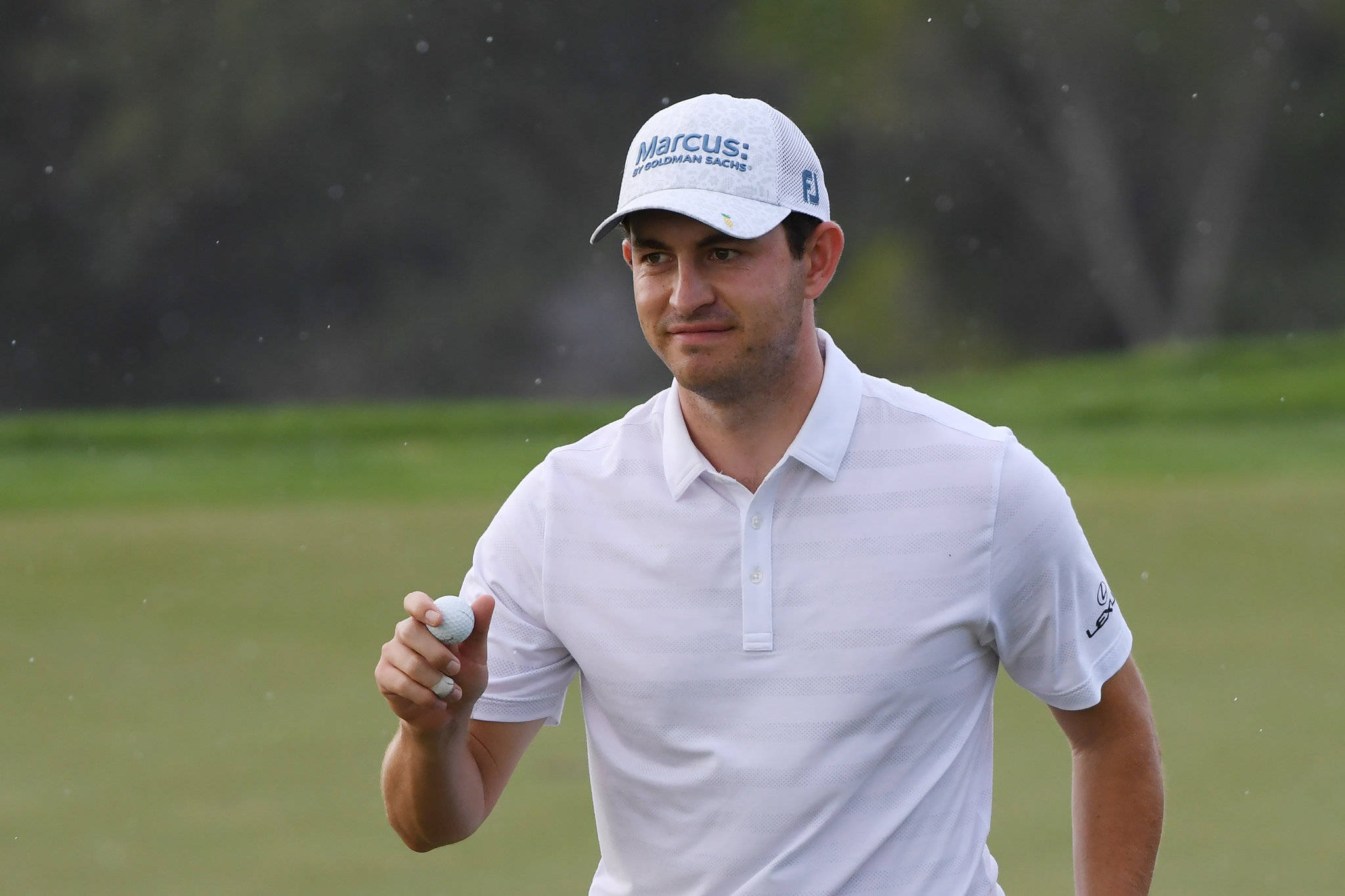 Pga 桌布 壁紙 — 戴白色帽子及穿白色Polo衫的高爾夫球手在綠色球場上，於細雨中手持高爾夫球，背景有模糊的樹木。