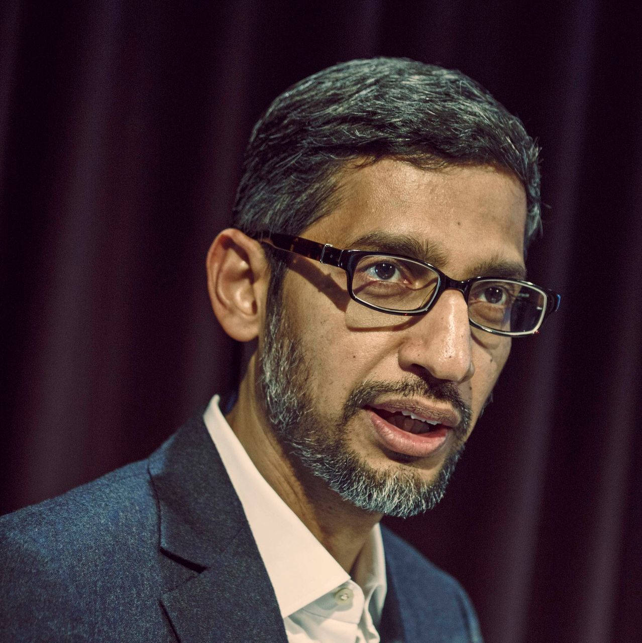 google 桌布 壁紙 — 戴眼鏡和鬍鬚的男子穿著西裝，以深色窗簾為背景的特寫肖像。
