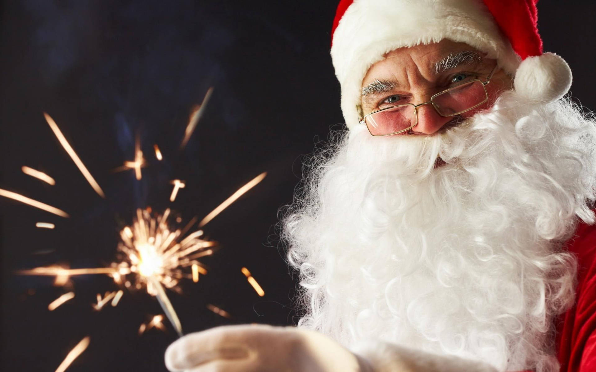 Santa Claus 桌布 壁紙 — 戴眼鏡的聖誕老人手持閃爍的煙火，背景漆黑。