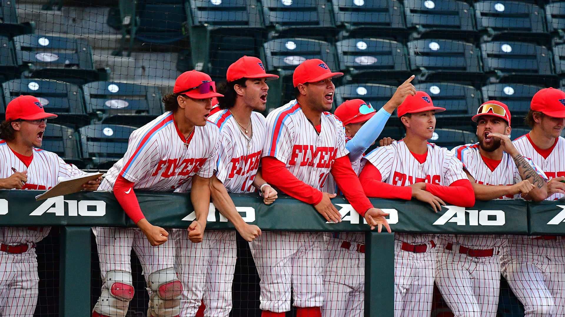 College Baseball 桌布 壁紙 — 戴紅色帽子、身穿白色細條紋球衣的棒球選手，在球員休息區的欄杆旁熱情歡呼。