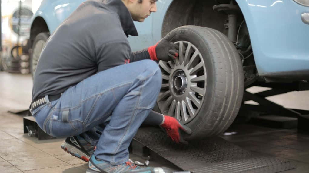 Winter Tires 桌布 壁紙 — 戴紅色手套的技工蹲下，從車庫升降台上的淺藍色汽車上拆下輪胎。