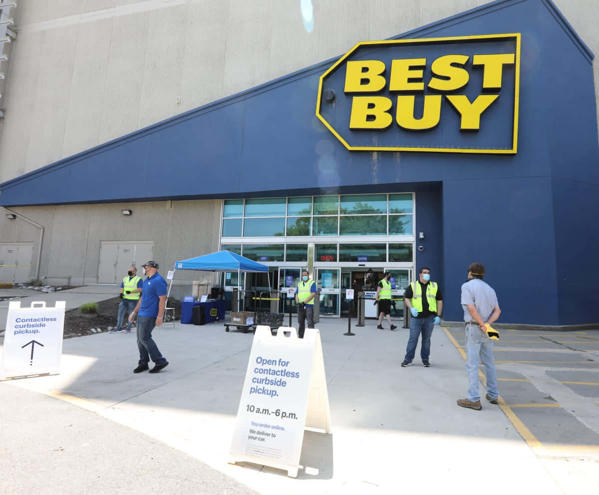 Best Buy 桌布 壁紙 — 戴著口罩和背心的人們在白天站在Best Buy商店外進行路邊取貨，有標誌和藍色帳篷。