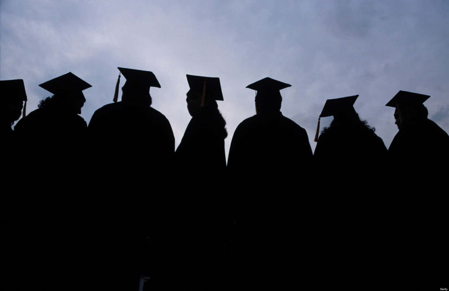 Graduation 桌布 壁紙 — 戴著學士帽和畢業袍的畢業生剪影，在多雲的黃昏天空下排成一排。