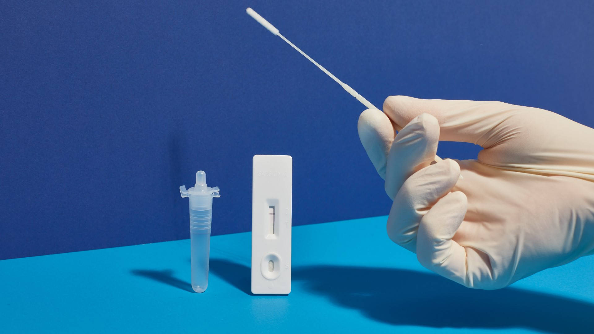 Medical 桌布 壁紙 — 戴著手套的手在鮮藍色表面上，將拭子懸停在COVID測試套件和小瓶上方。