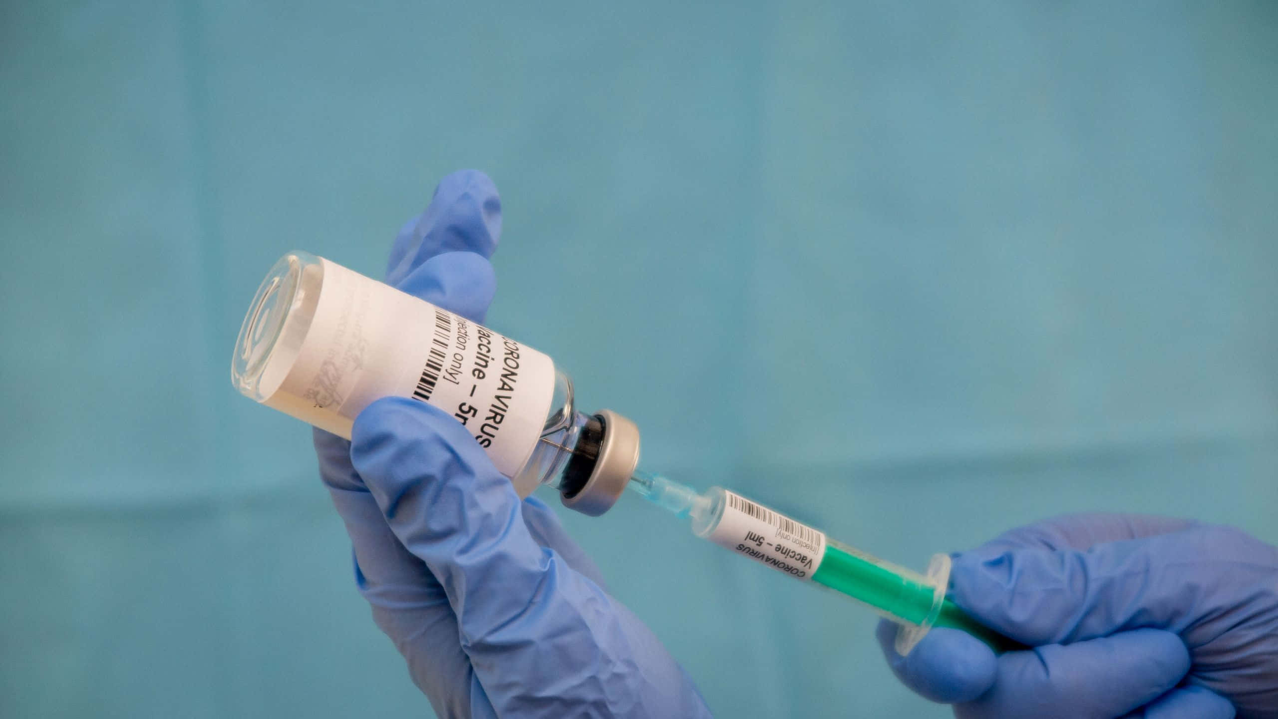 injection 桌布 壁紙 — 戴著手套的手小心地從有標籤的小瓶中抽取綠色疫苗液體，背景是青綠色的醫療背景。