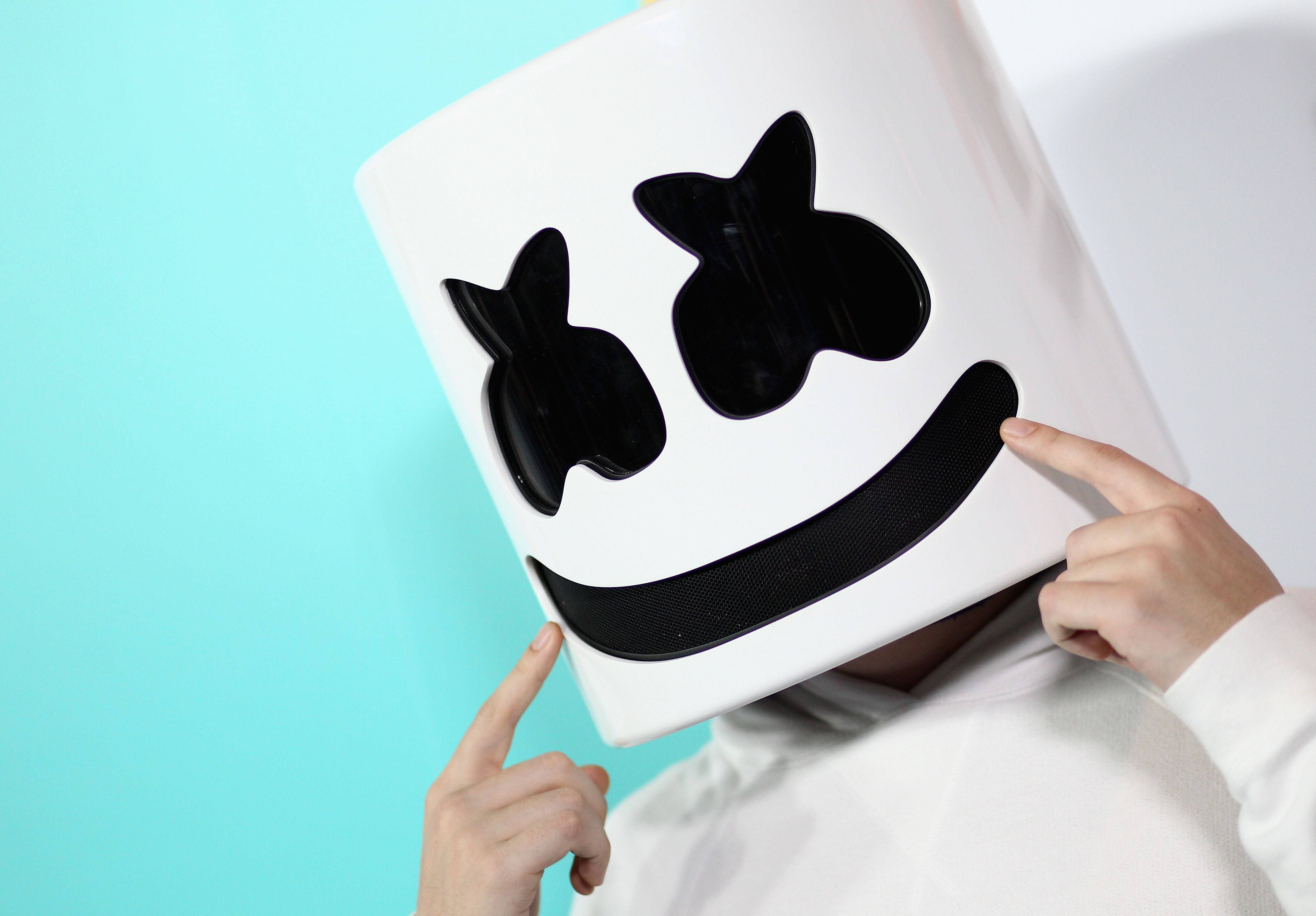 Marshmallow Dj 桌布 壁紙 — 戴著標誌性白色Marshmello頭盔、帶黑色笑臉的人，在藍綠色背景下指著頭盔。