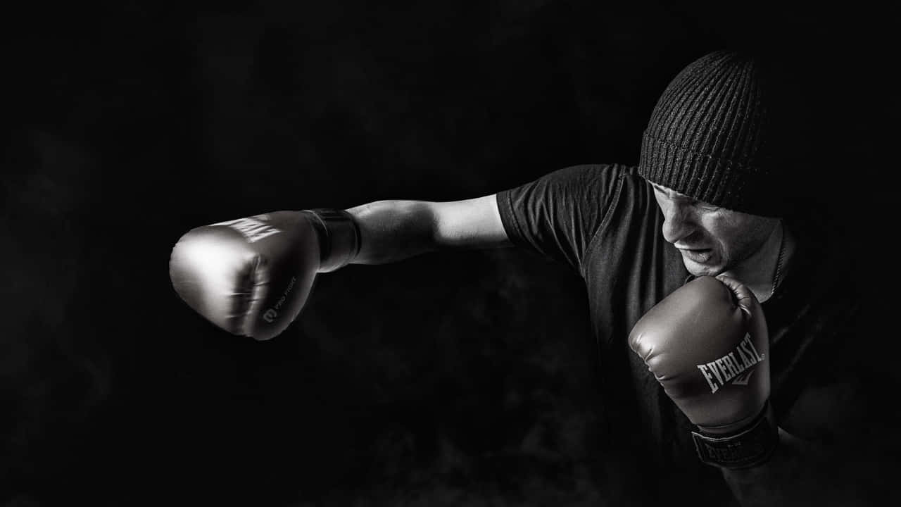 運動 桌布 壁紙 — 戴著毛帽的拳擊手在戲劇性的黑白畫面中出拳，煙霧在他周圍旋轉。