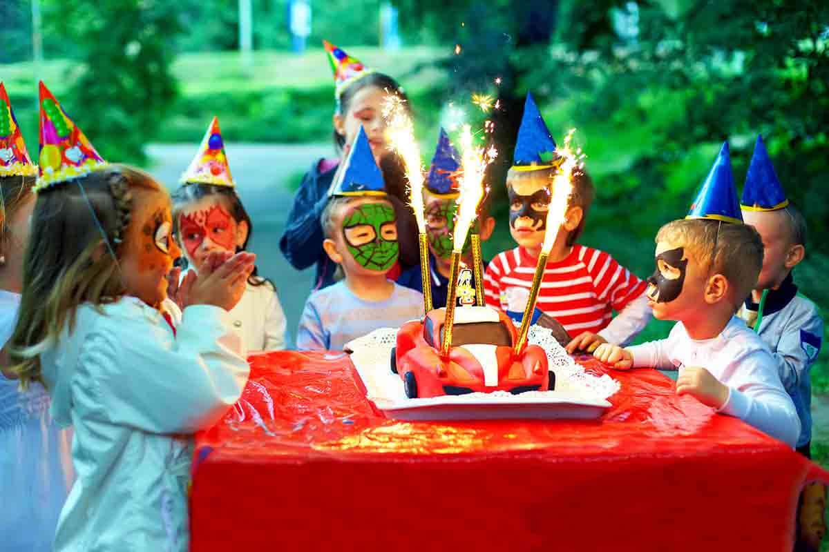 Birthday Party 桌布 壁紙 — 戴著派對帽和臉部彩繪的孩子們聚集在紅色汽車蛋糕周圍，煙火照亮了歡樂的戶外生日場景。