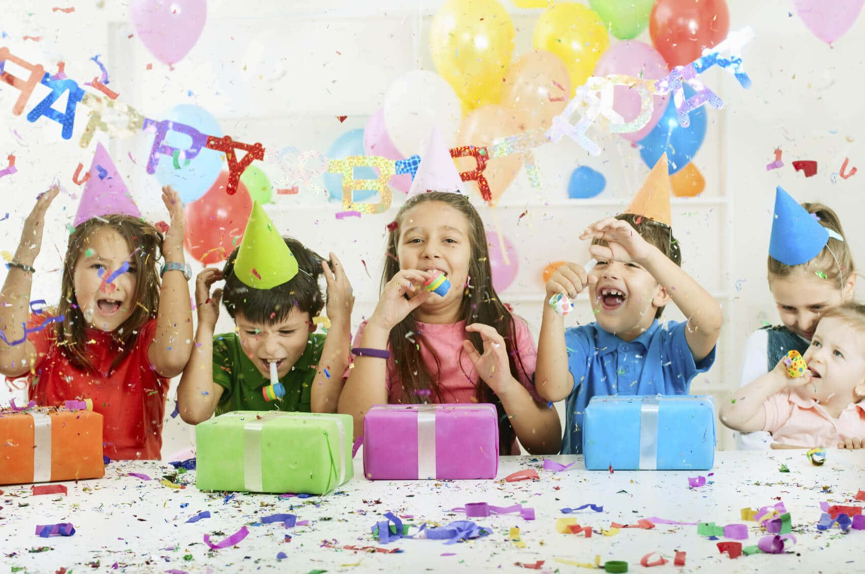 Birthday Party 桌布 壁紙 — 戴著派對帽的孩子們在生日派對上笑著慶祝，周圍有五彩紙屑氣球和色彩繽紛的禮物。