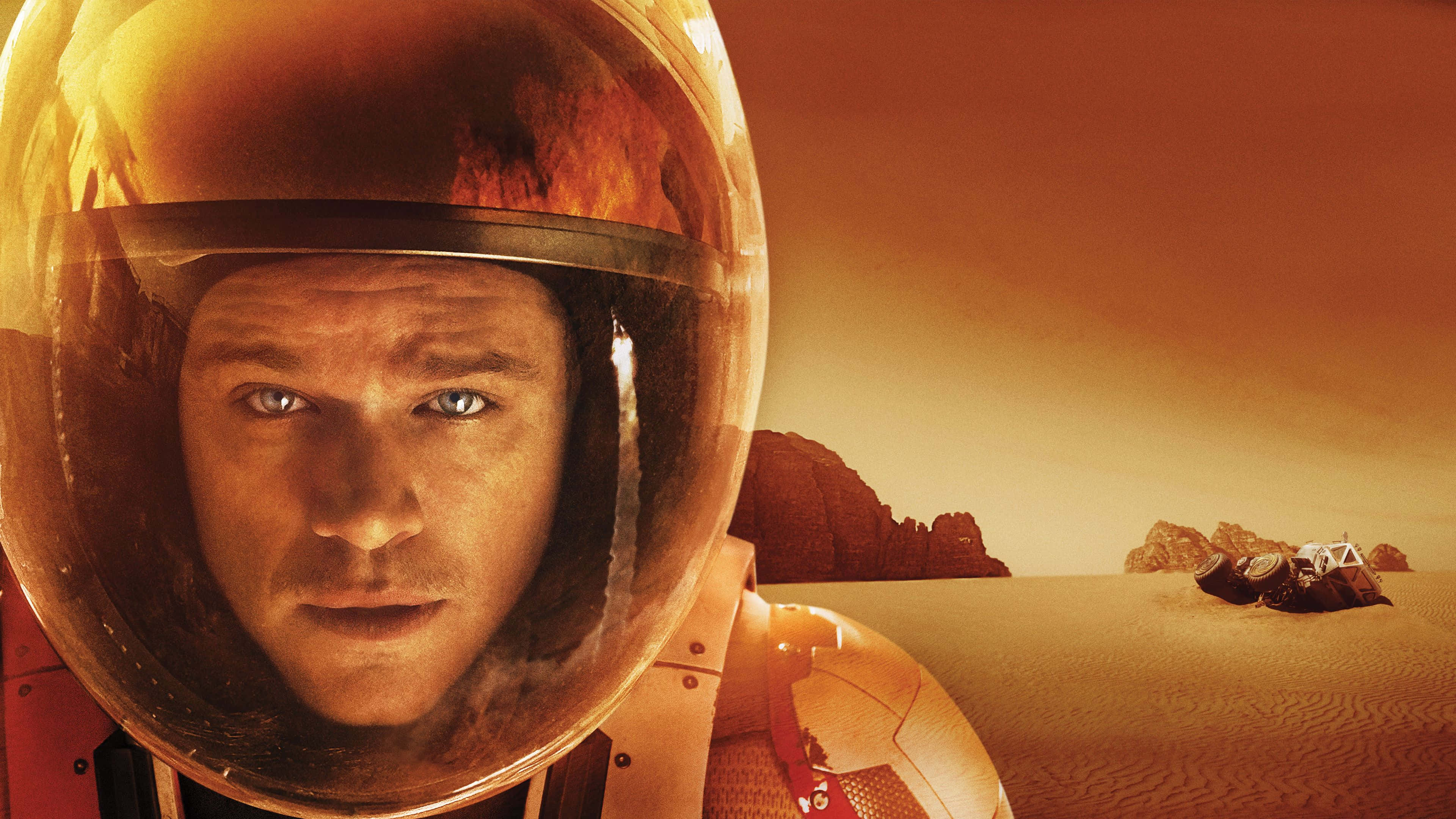 The Martian 桌布 壁紙 — 戴著頭盔的太空人在溫暖的橙色霧氣中，從火星表面與探測車和岩石地形一起專注地凝視。