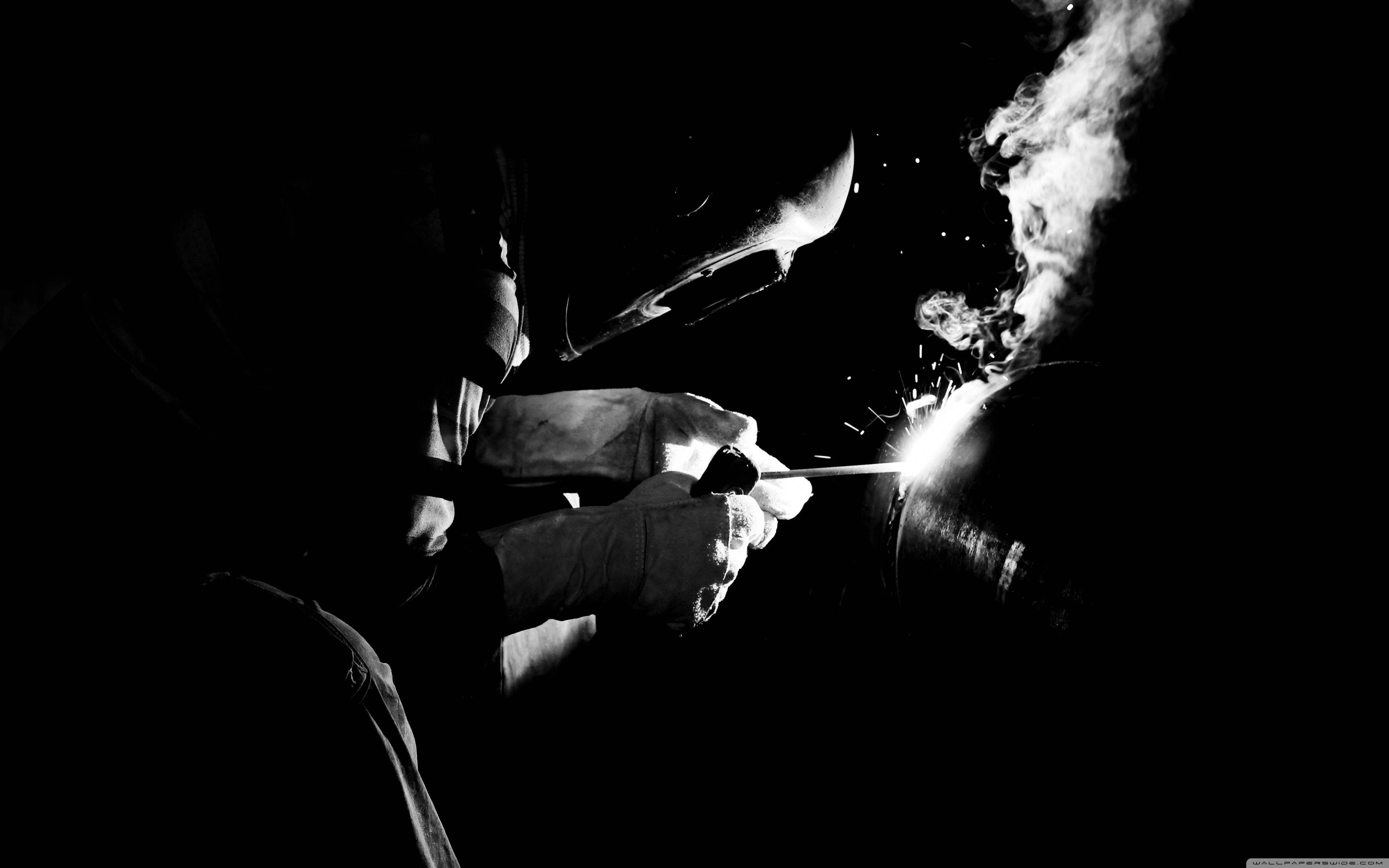 煙動圖 桌布 壁紙 — 戴著頭盔的焊工在黑暗背景下產生明亮的火花，熱金屬冒出的煙霧升騰。