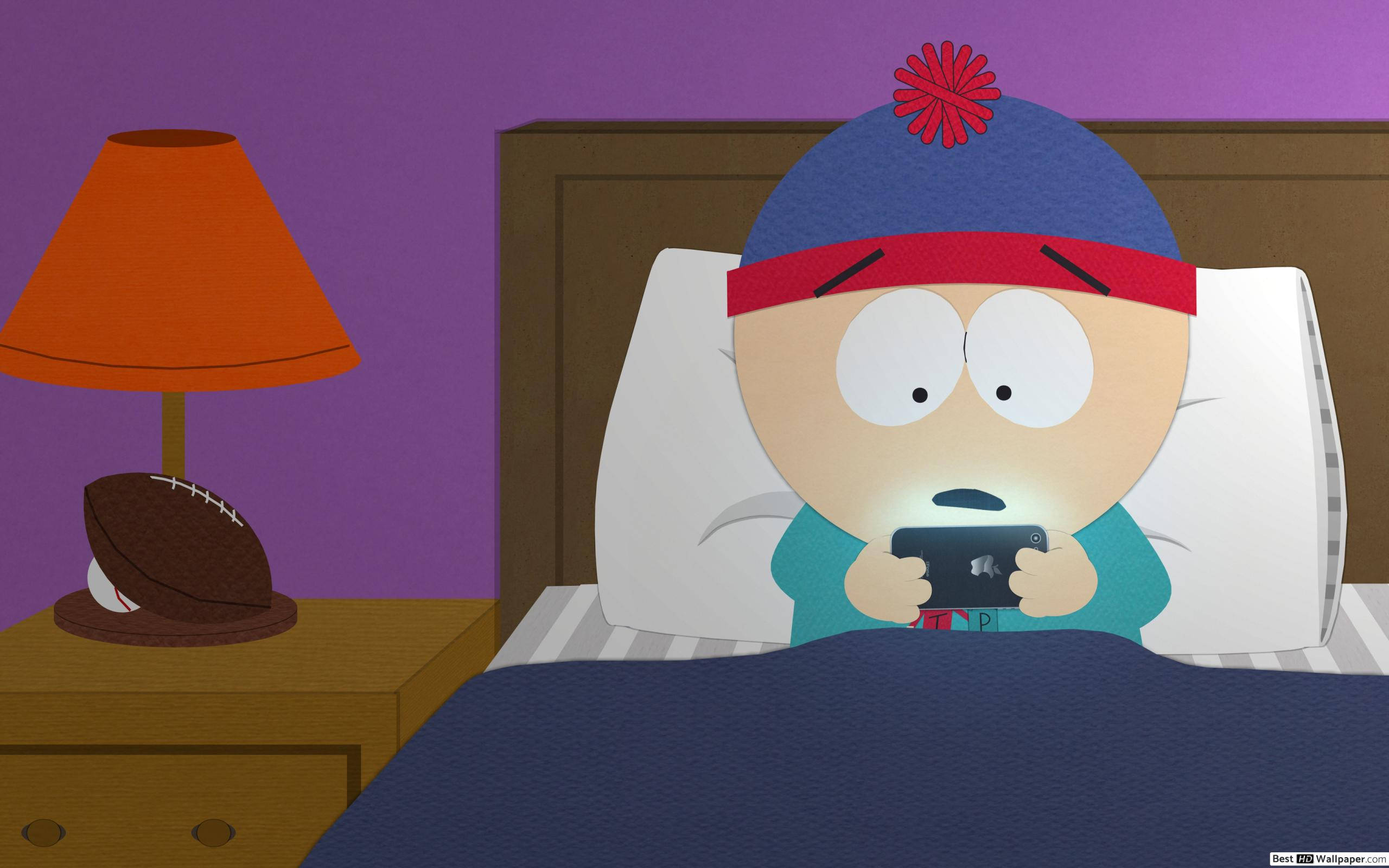 stan marsh 桌布 壁紙 — 戴藍色帽子的卡通男孩躺在床上蓋著被子，手中拿著發光的手機，紫色牆壁，橙色燈，床頭櫃上有足球。