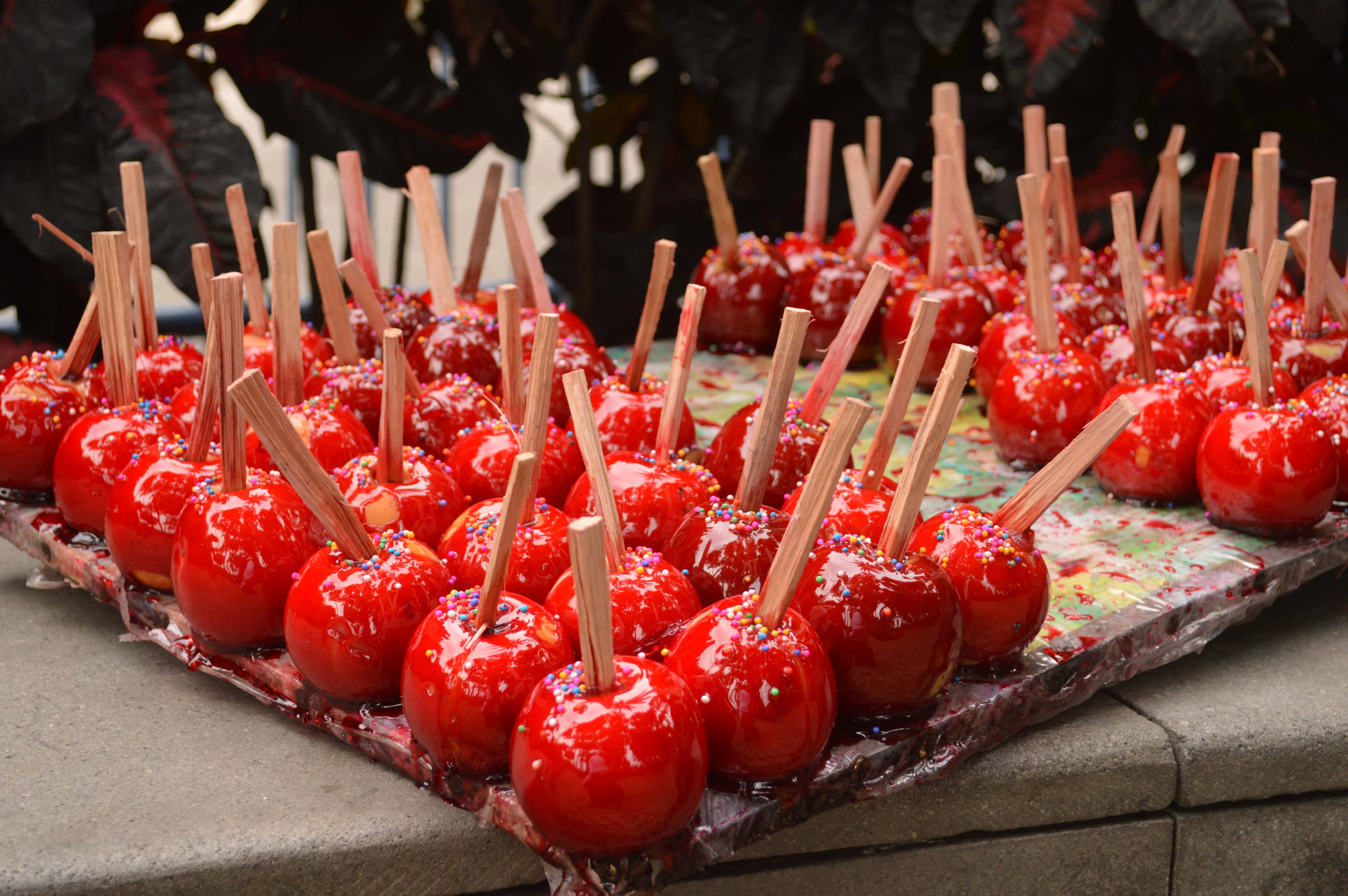 Candy Apples 桌布 壁紙 — 戶外托盤上排列著一排排閃亮的紅色糖果蘋果，插著棒子，撒上彩色糖粒。