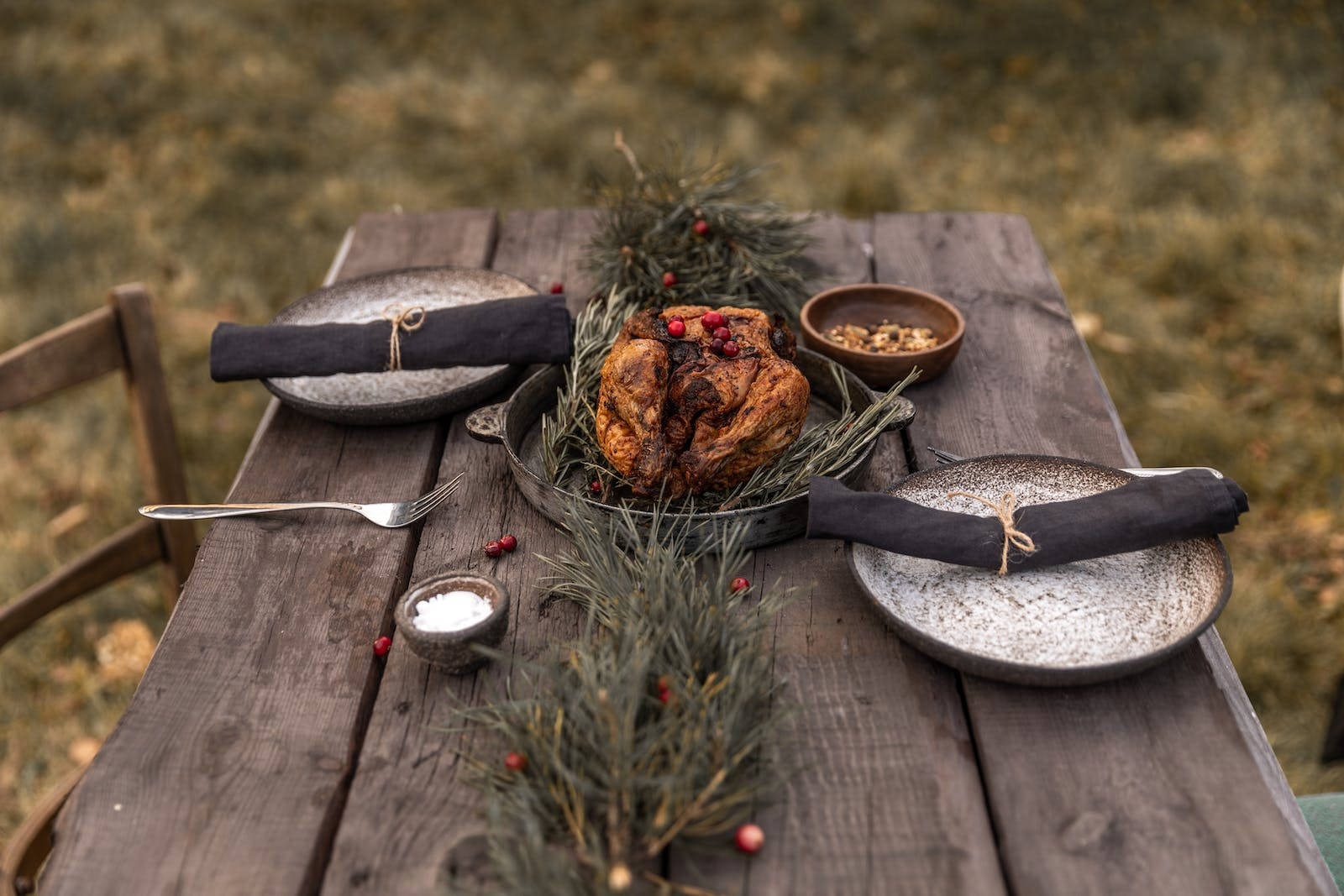 Thanksgiving Day 桌布 壁紙 — 戶外擺放著一張質樸的木桌，桌上有一隻烤火雞，以迷迭香和紅色漿果裝飾，周圍放著陶瓷盤子和碗。