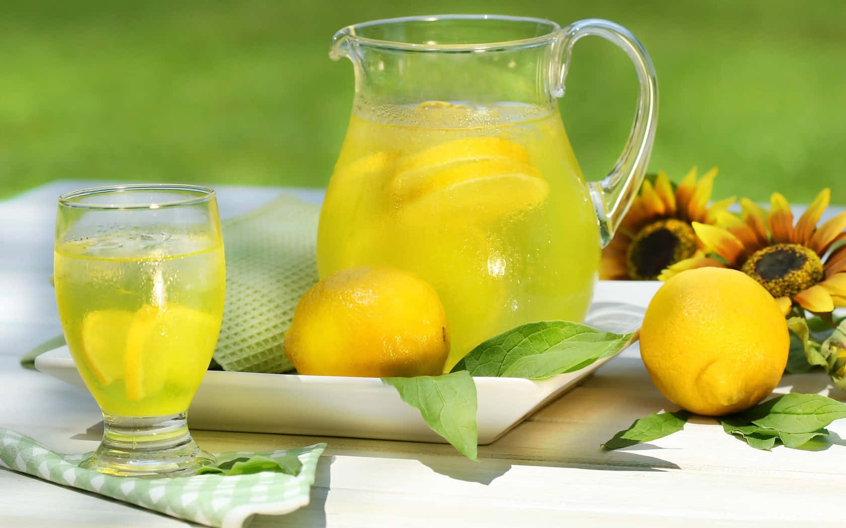 Refreshing 桌布 壁紙 — 戶外白色木桌上，一杯及一壺清涼檸檬水，配以整顆檸檬和向日葵。