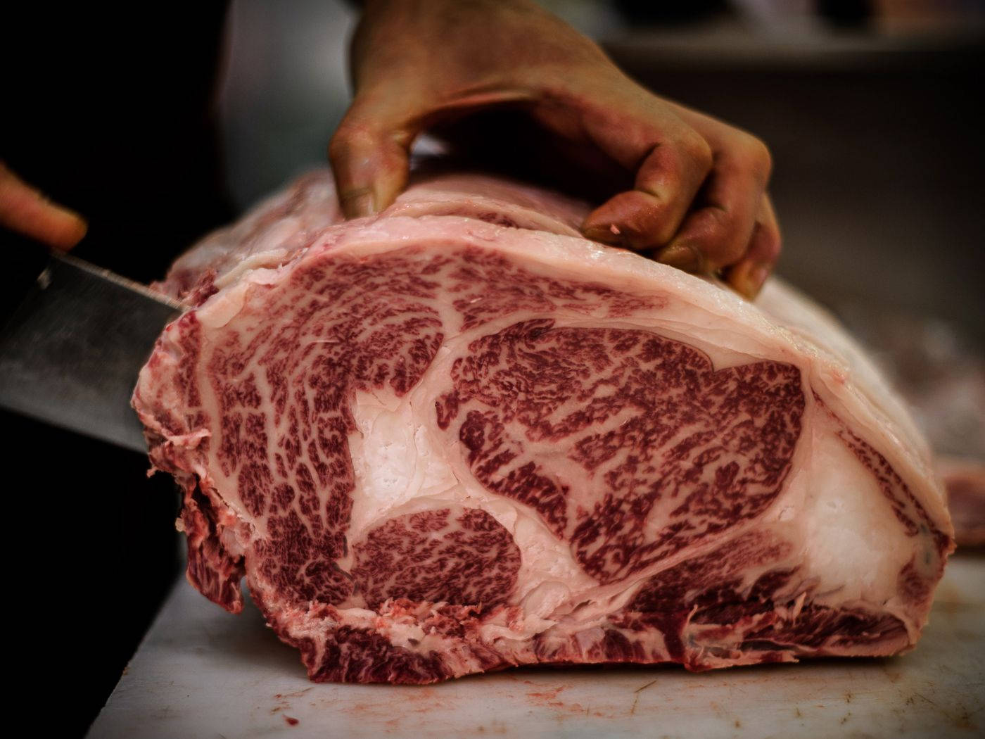 meat 桌布 壁紙 — 手切開大理石紋牛肉的特寫，露出豐富的紅肉和白色脂肪。