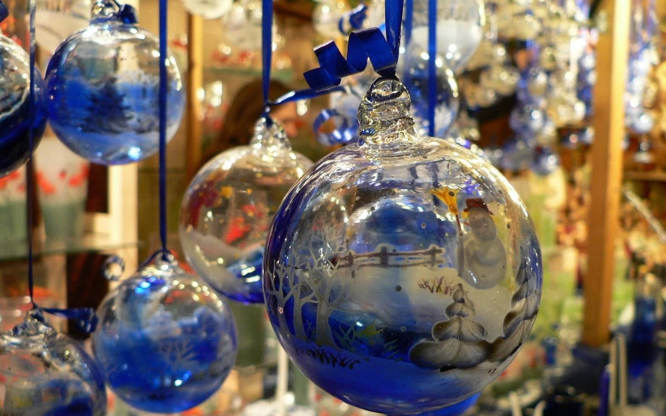 balls 桌布 壁紙 — 手吹玻璃裝飾品，繪有冬季場景，懸掛在節日商店中，透過半透明的藍色表面捕捉溫暖光線。