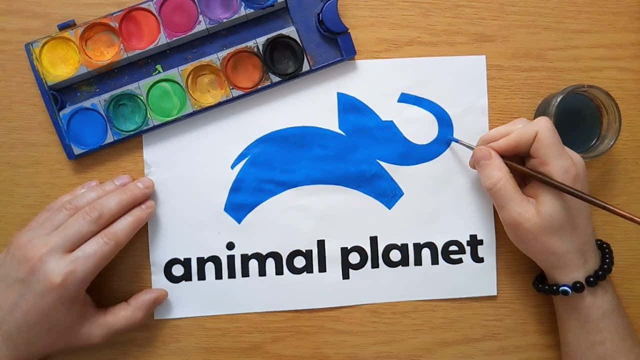 動物星球 桌布 壁紙 — 手在木桌上用水彩調色板和畫筆旁邊的紙上畫一個藍色大象標誌。