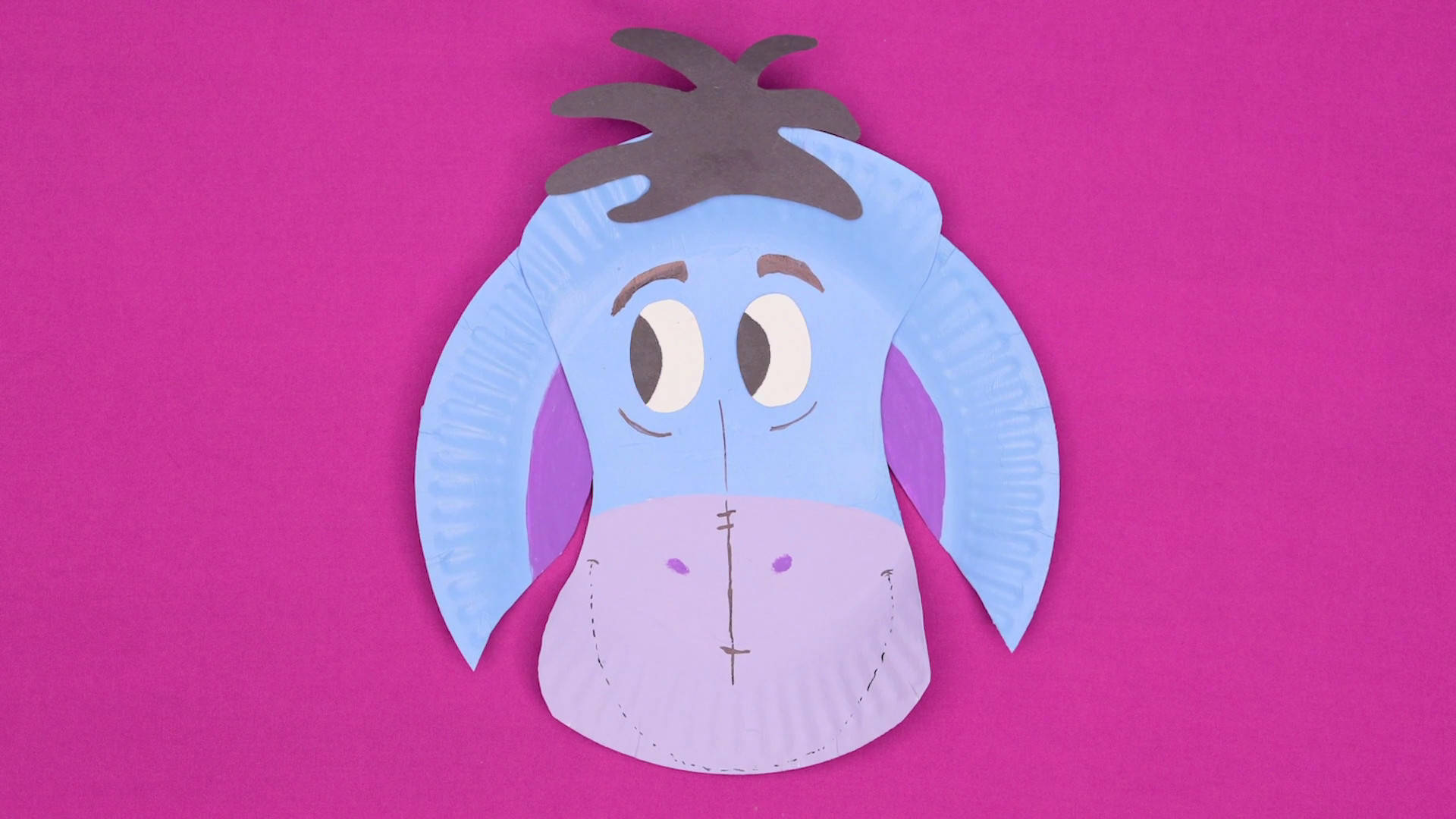 Eeyore 桌布 壁紙 — 手工紙盤工藝品，以屹耳為主題，藍色耳朵和紫色鼻子，襯托鮮豔的粉紅色背景。