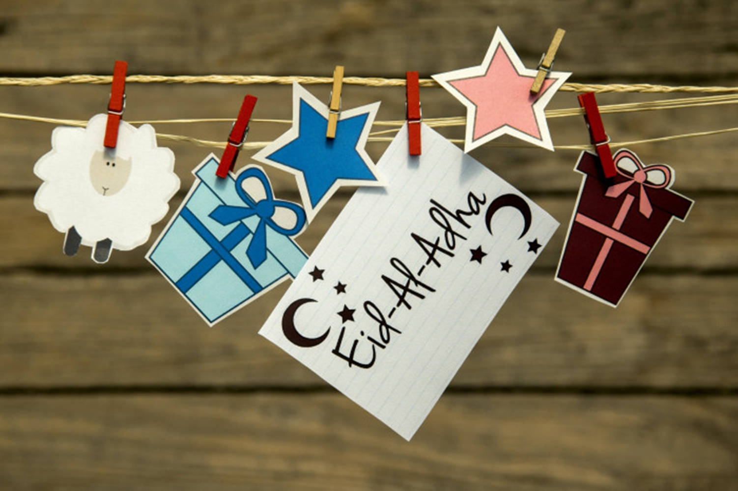 Stars 桌布 壁紙 — 手工紙裝飾品，包括羊、星星、禮物和Eid Al Adha卡片，掛在繩子上，背景為木質。