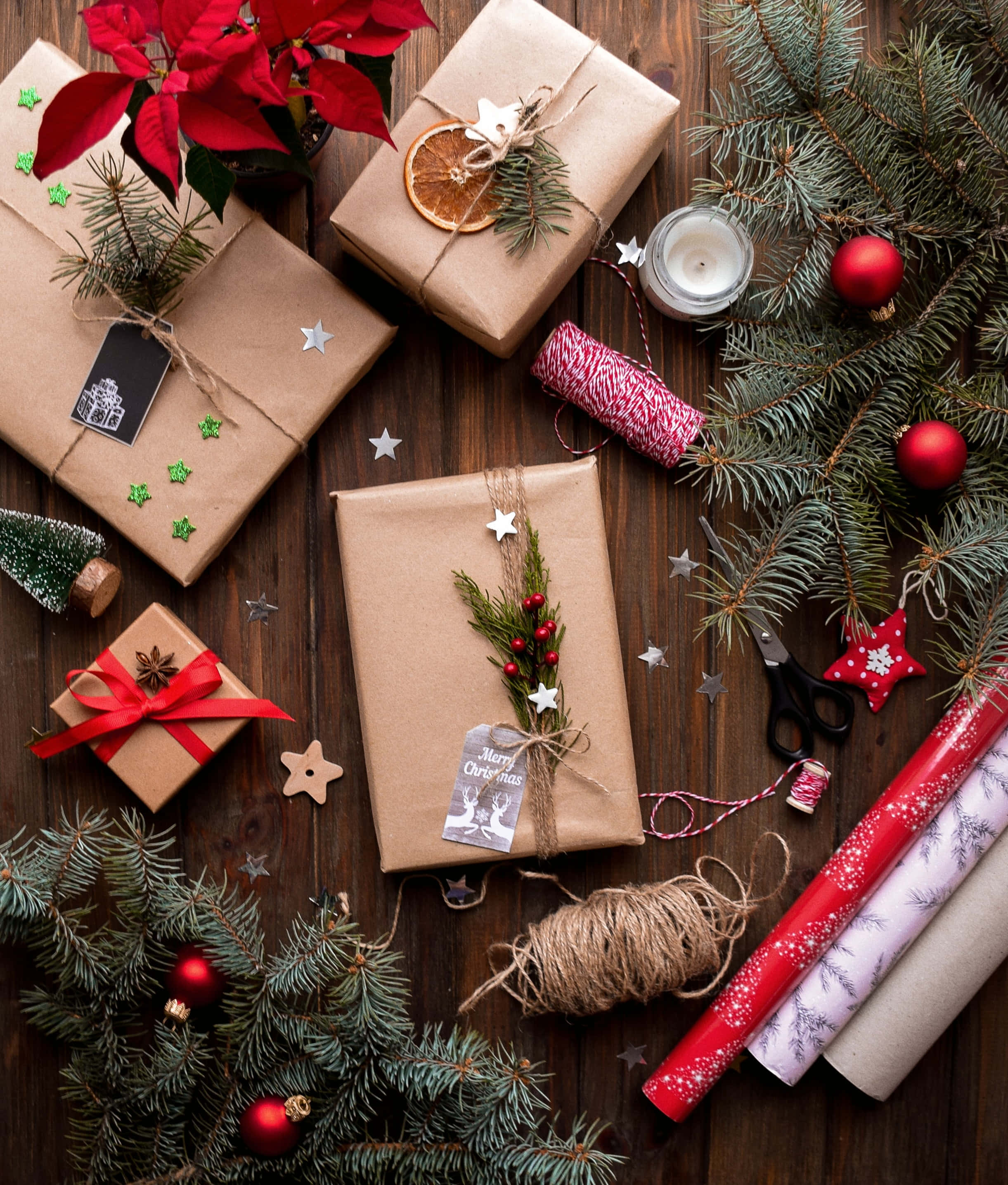 Christmas Scene 桌布 壁紙 — 手工聖誕禮物用牛皮紙和麻繩包裝，松枝和紅色裝飾品散落在鄉村風木桌上。