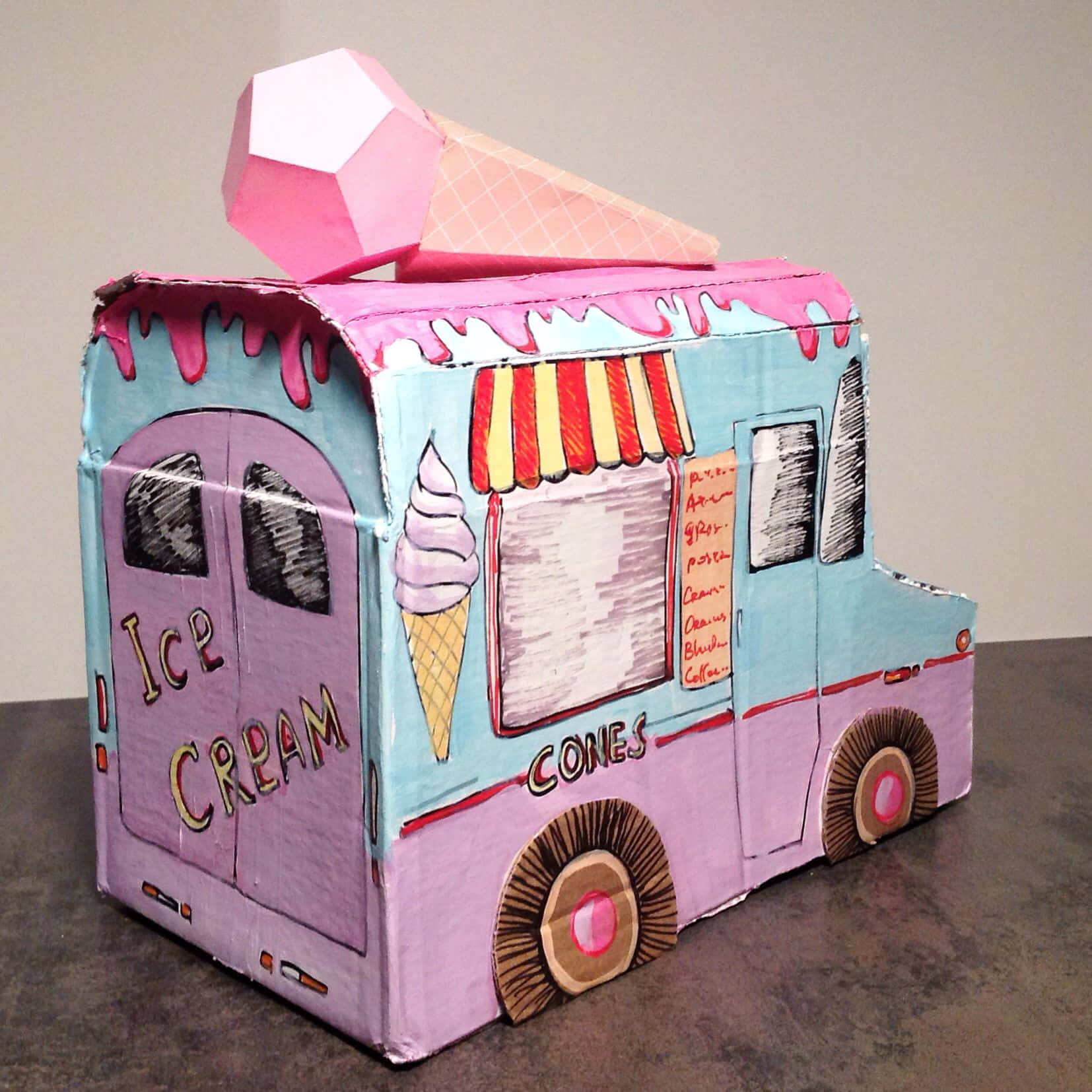 Ice Cream Truck 桌布 壁紙 — 手工製作的紙板冰淇淋車，塗上粉紅色和藍色，帶有滴落的粉紅色糖霜，頂部有一個巨大的粉紅色冰淇淋甜筒。