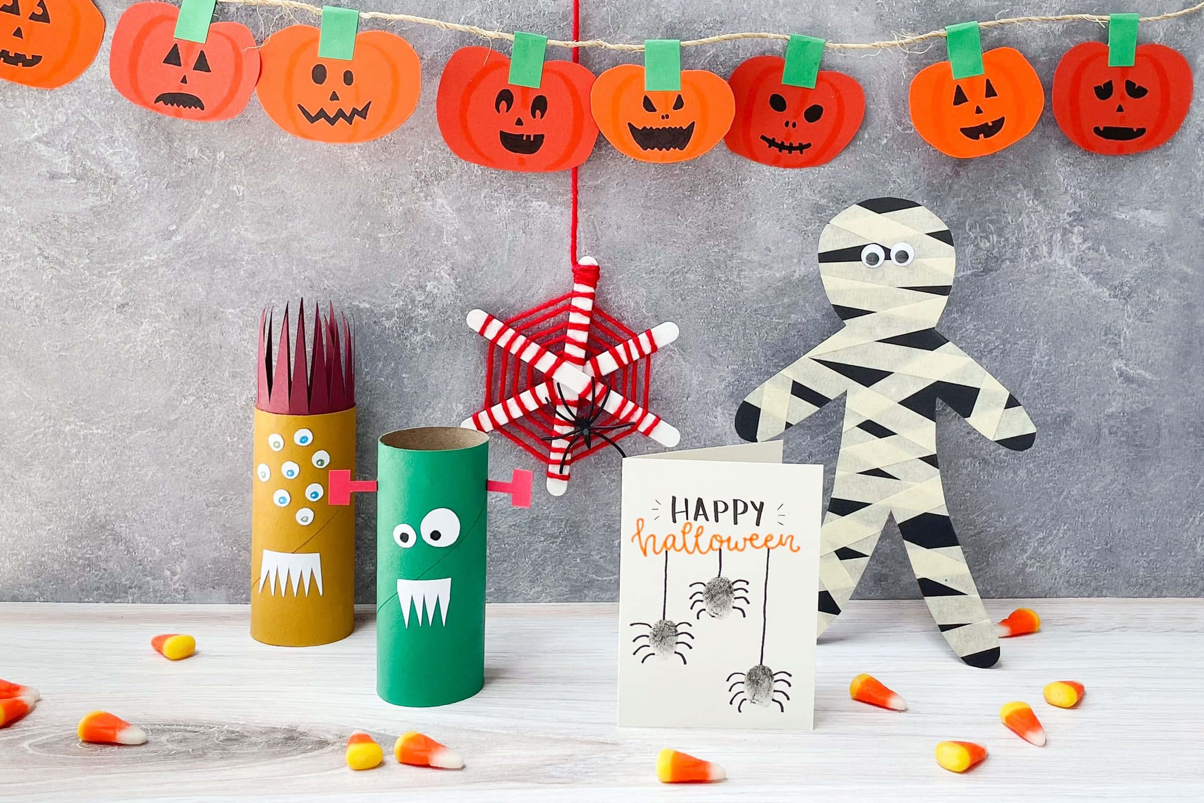 Halloween Props 桌布 壁紙 — 手工製作的萬聖節裝飾，包括用紙板筒製作的南瓜、木乃伊和怪物，以及散落在木質表面上的玉米糖。