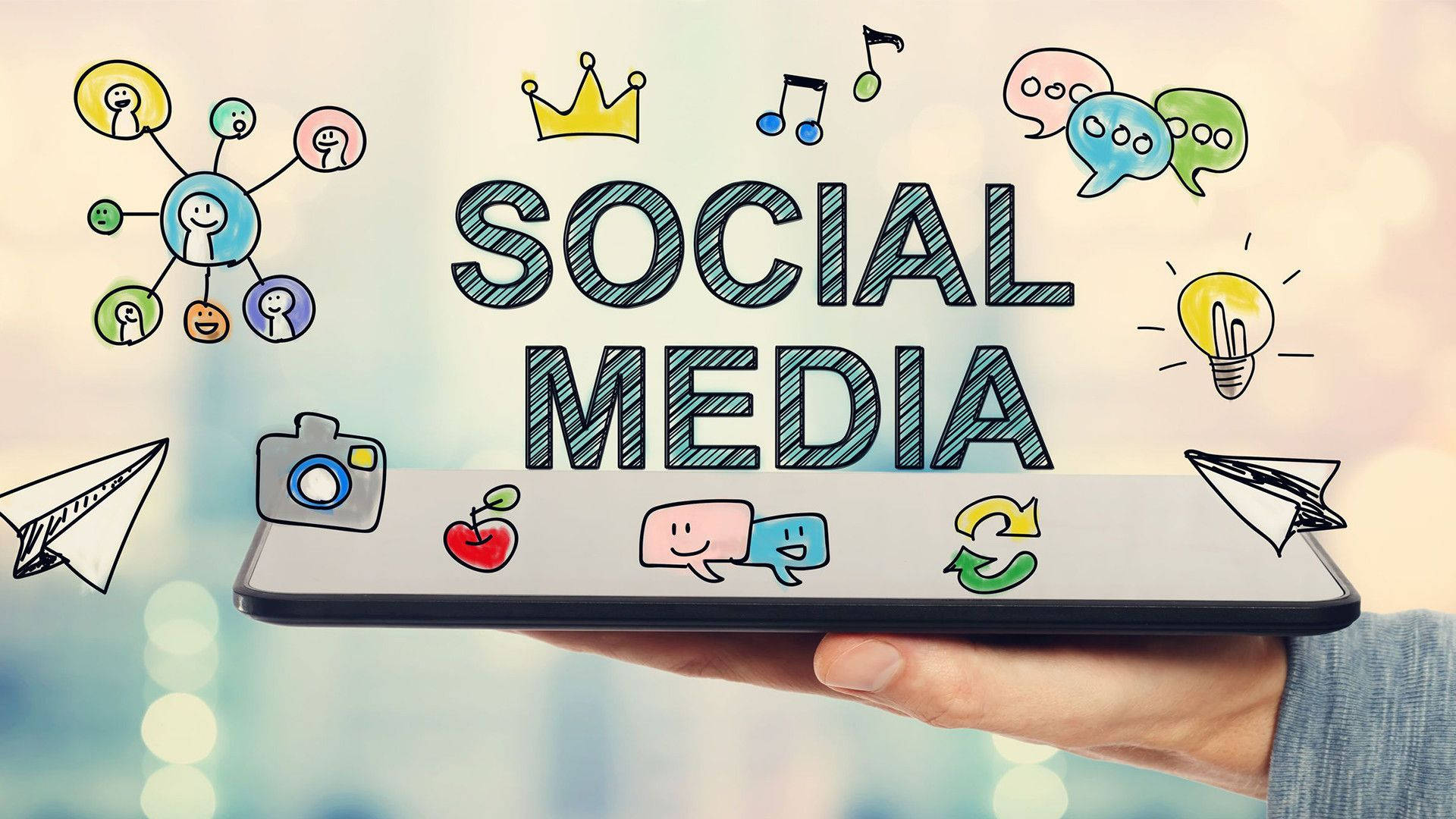 Social 桌布 壁紙 — 手拿著智慧型手機，顯示 'SOCIAL MEDIA'，周圍有塗鴉圖標漂浮在模糊背景上。
