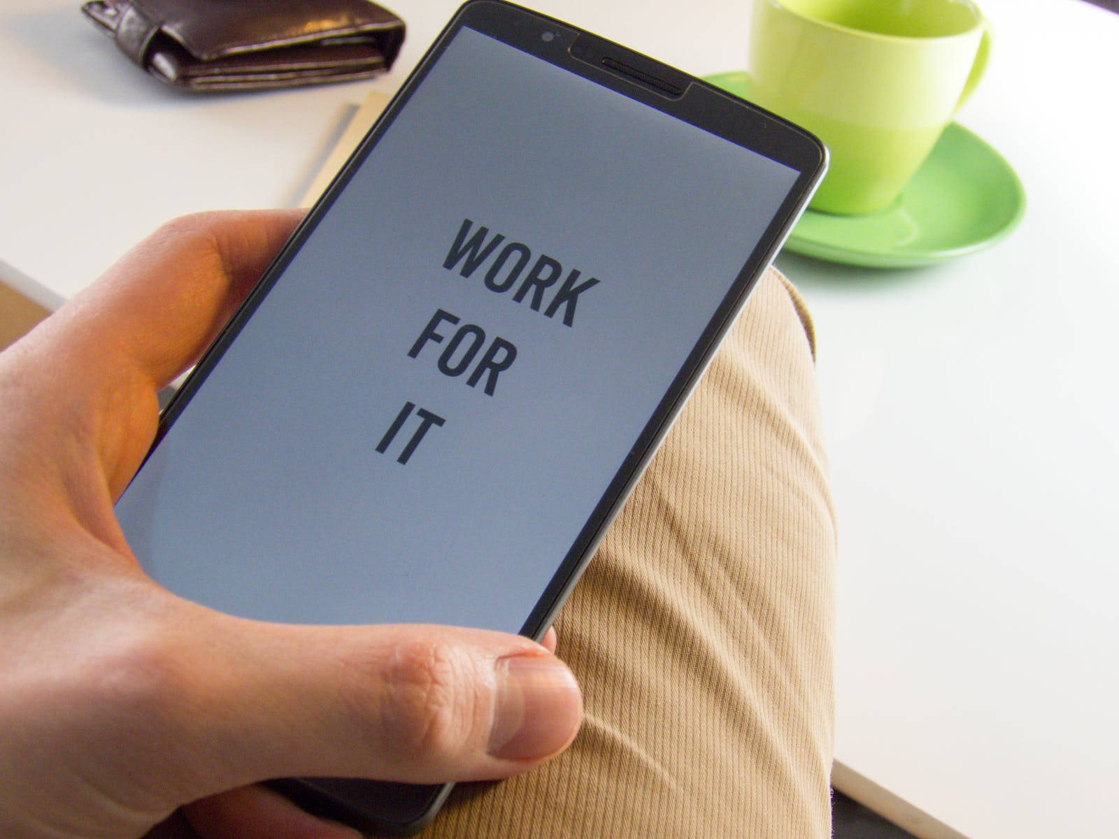 Motivation 桌布 壁紙 — 手拿著智慧型手機顯示 'WORK FOR IT' 文字，坐著時旁邊有綠色咖啡杯和錢包。