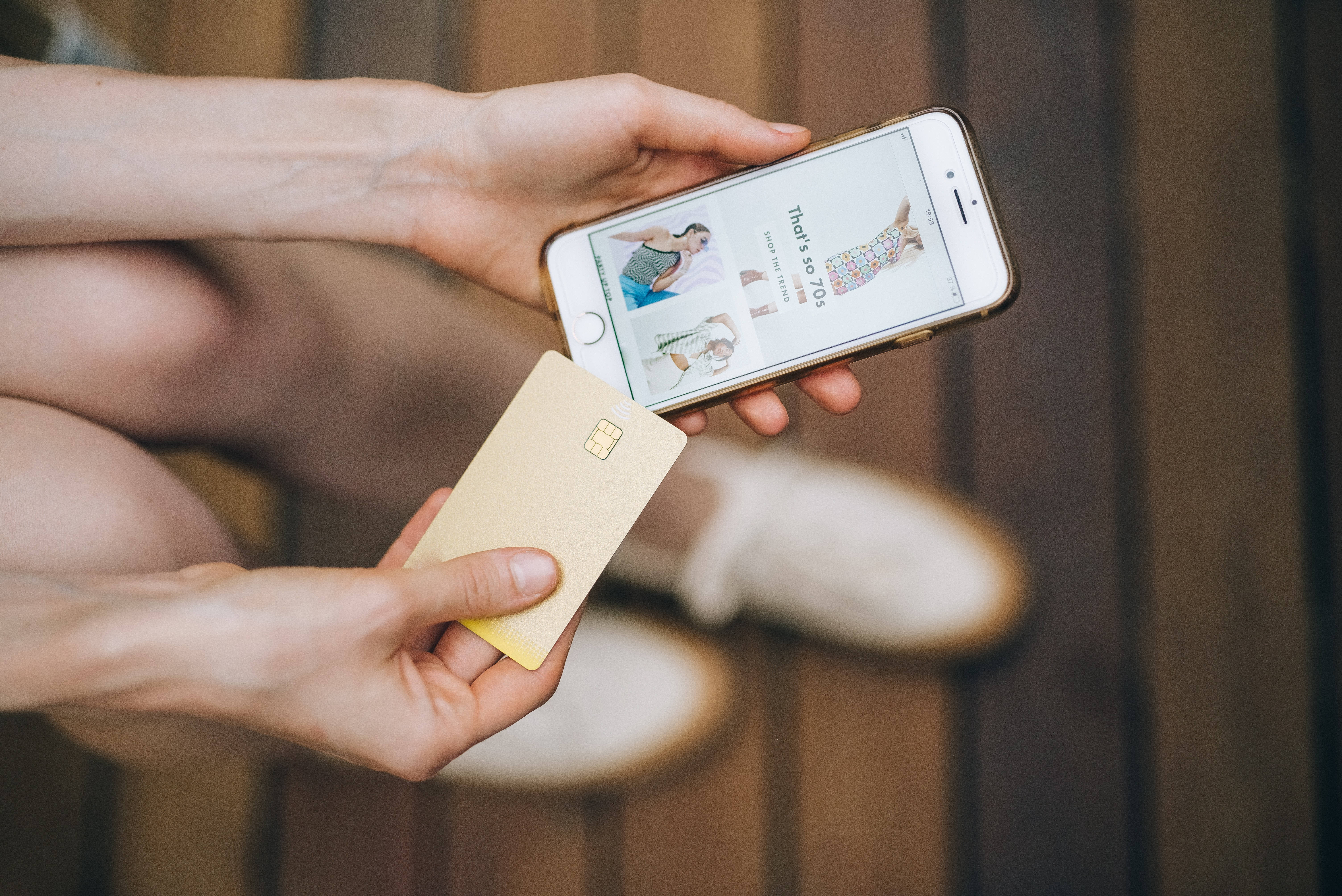 iPhone 桌布 壁紙 — 手持智慧型手機顯示時尚物品和金色信用卡進行線上購物的特寫。