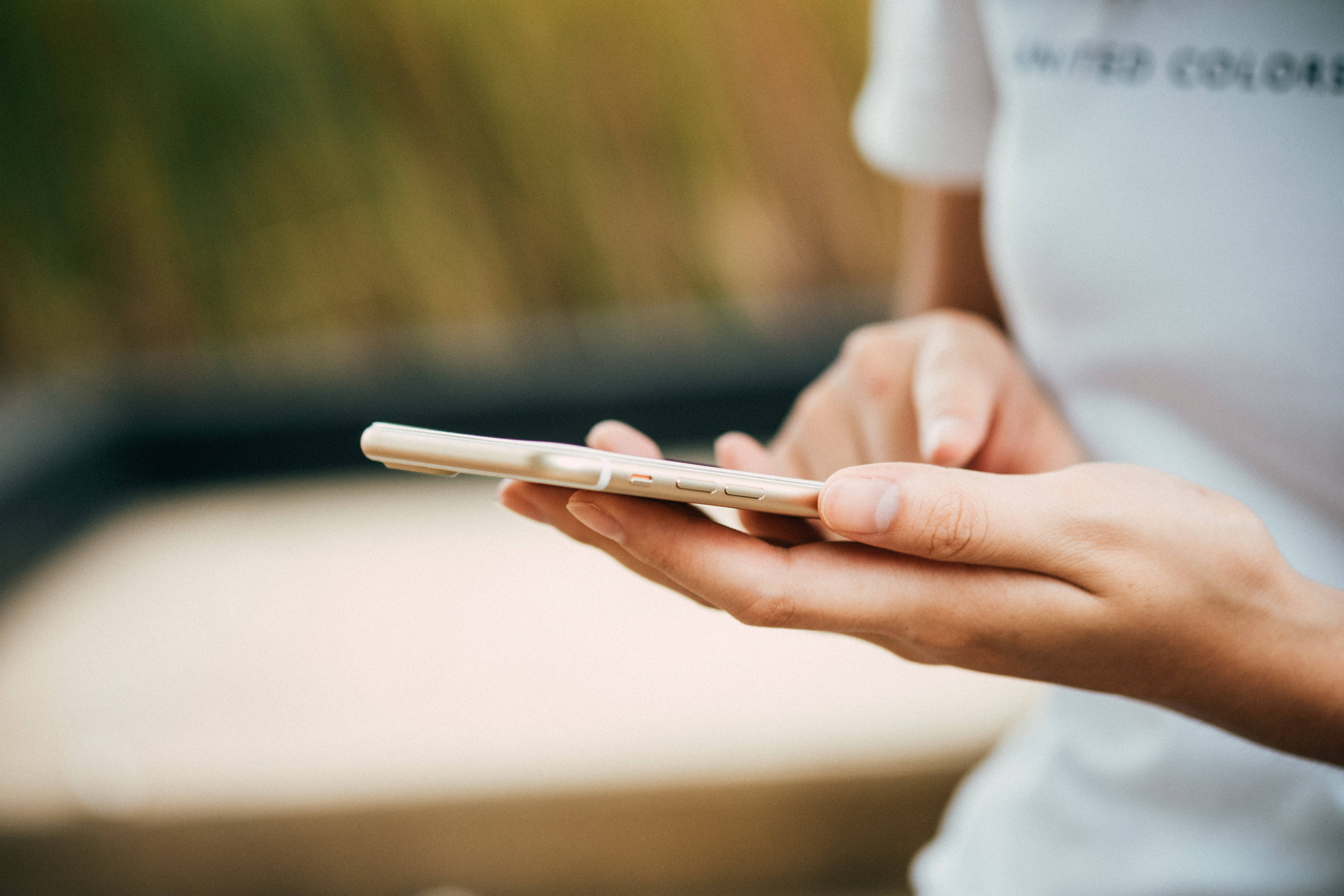 酷炫iPhone 桌布 壁紙 — 手持金色智慧型手機的特寫，背景模糊的戶外環境。