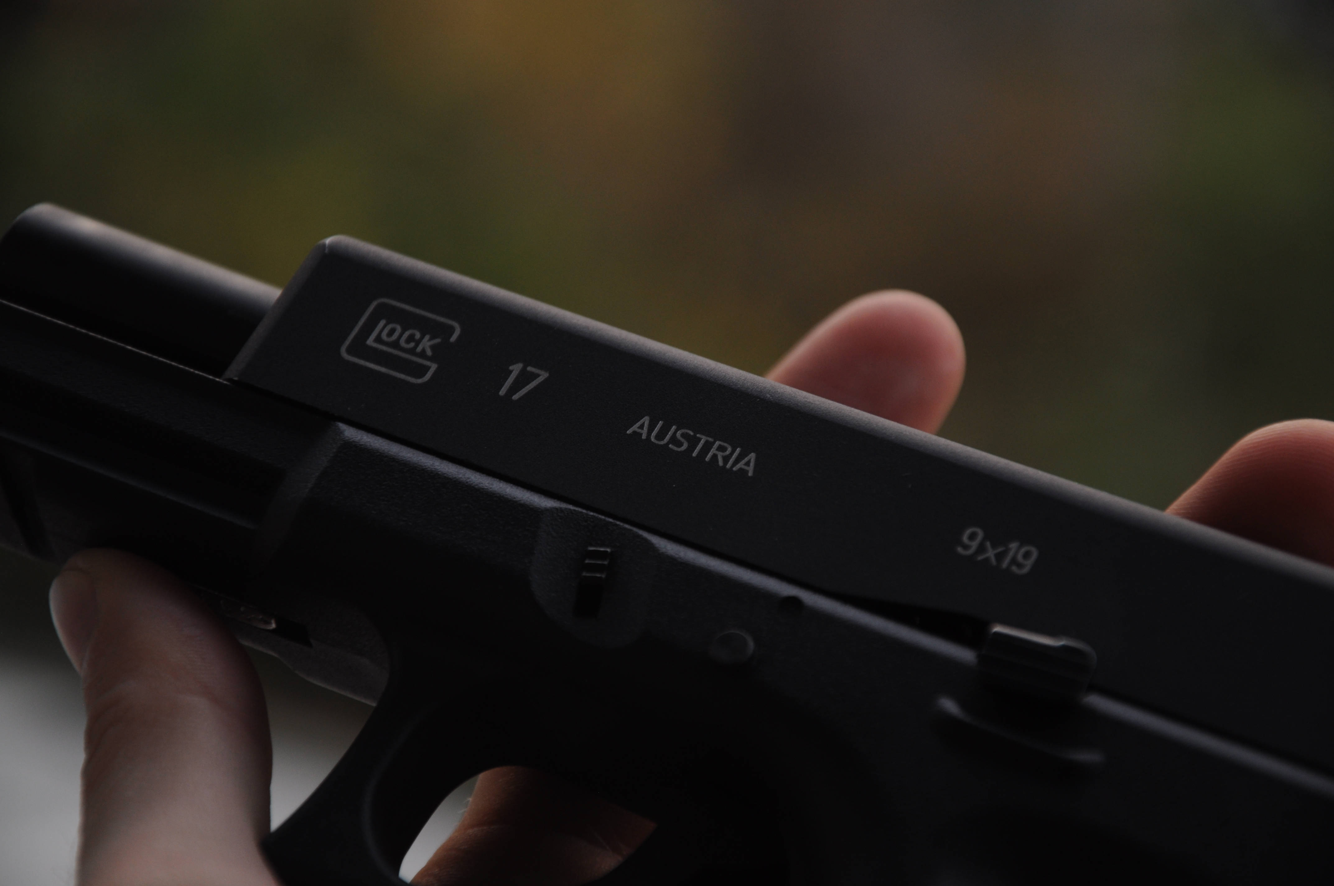 Glock 桌布 壁紙 — 手持黑色 Glock 17 手槍的特寫，背景模糊的秋景。