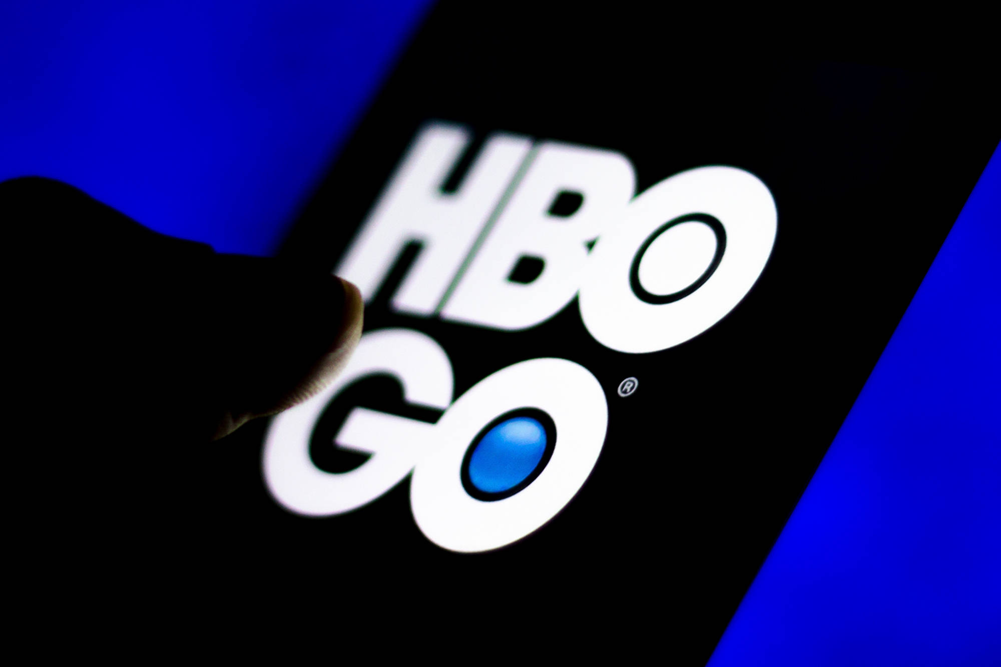HBO 桌布 壁紙 — 手指在深藍色背景上輕觸智慧型手機螢幕上發光的HBO GO標誌。