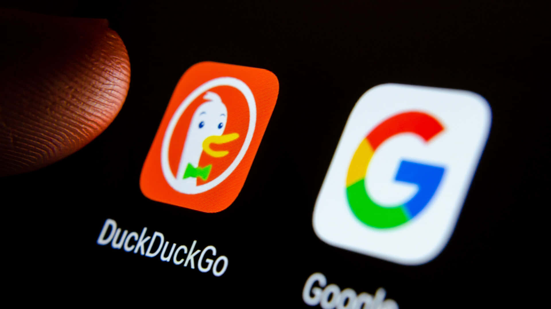 Duckduckgo 桌布 壁紙 — 手指懸浮在智慧型手機螢幕上Google旁邊的DuckDuckGo應用程式圖示上的特寫。
