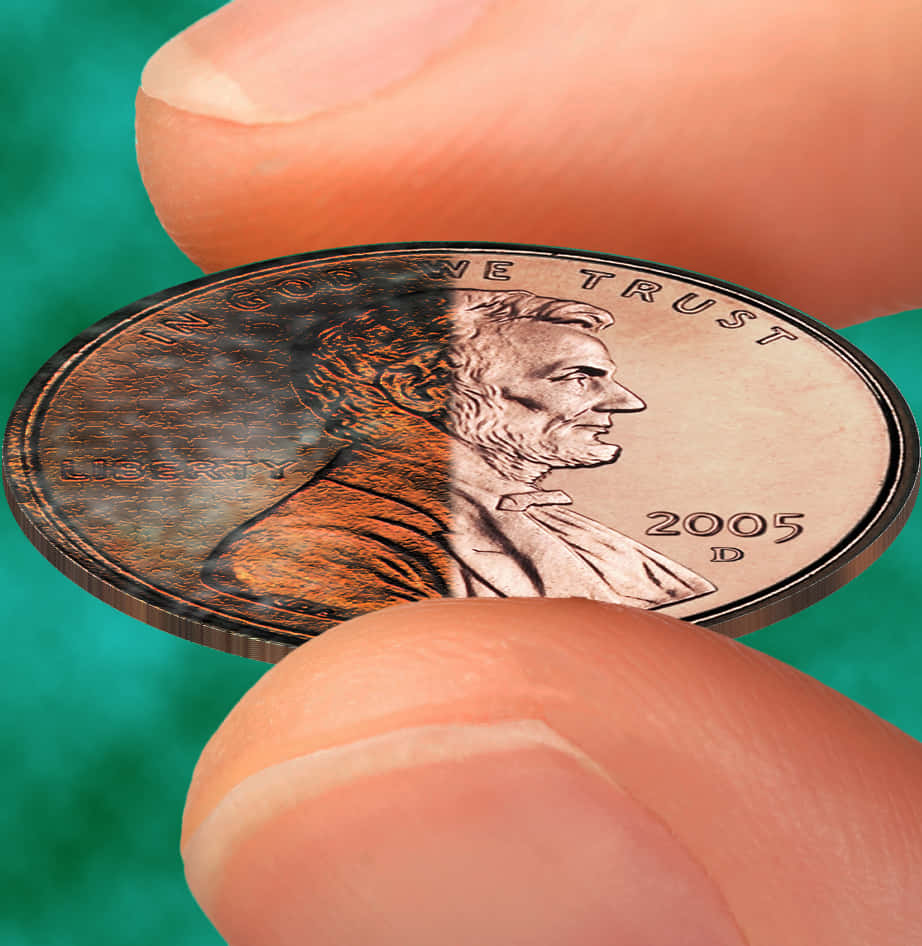 Coin 桌布 壁紙 — 手指拿著一枚2005年D林肯便士的特寫，一半生鏽一半完好，背景為青綠色。