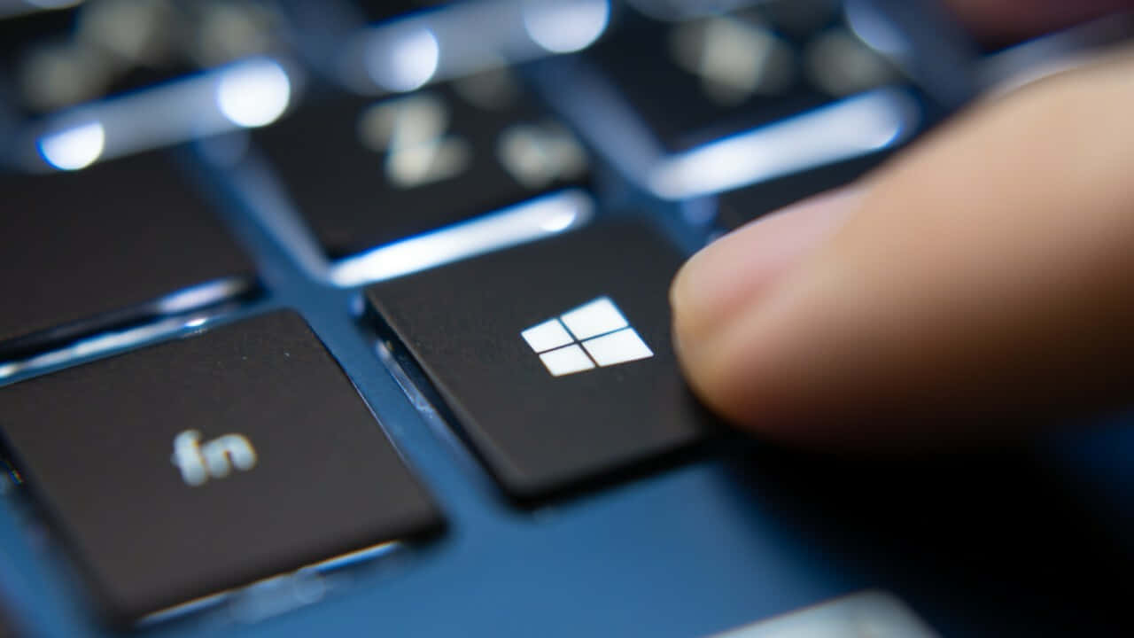 Cool Windows Desktop 桌布 壁紙 — 手指按下光滑黑色鍵盤上Windows鍵的特寫，帶有發光反射。