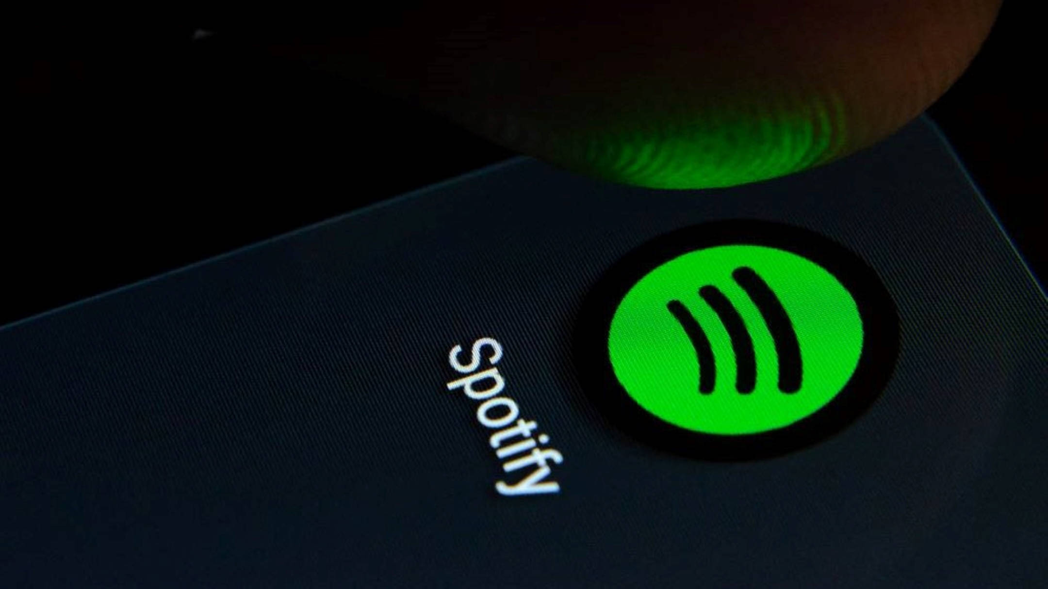 Spotify 桌布 壁紙 — 手指按壓黑暗智慧型手機螢幕上發光的綠色Spotify標誌的特寫。